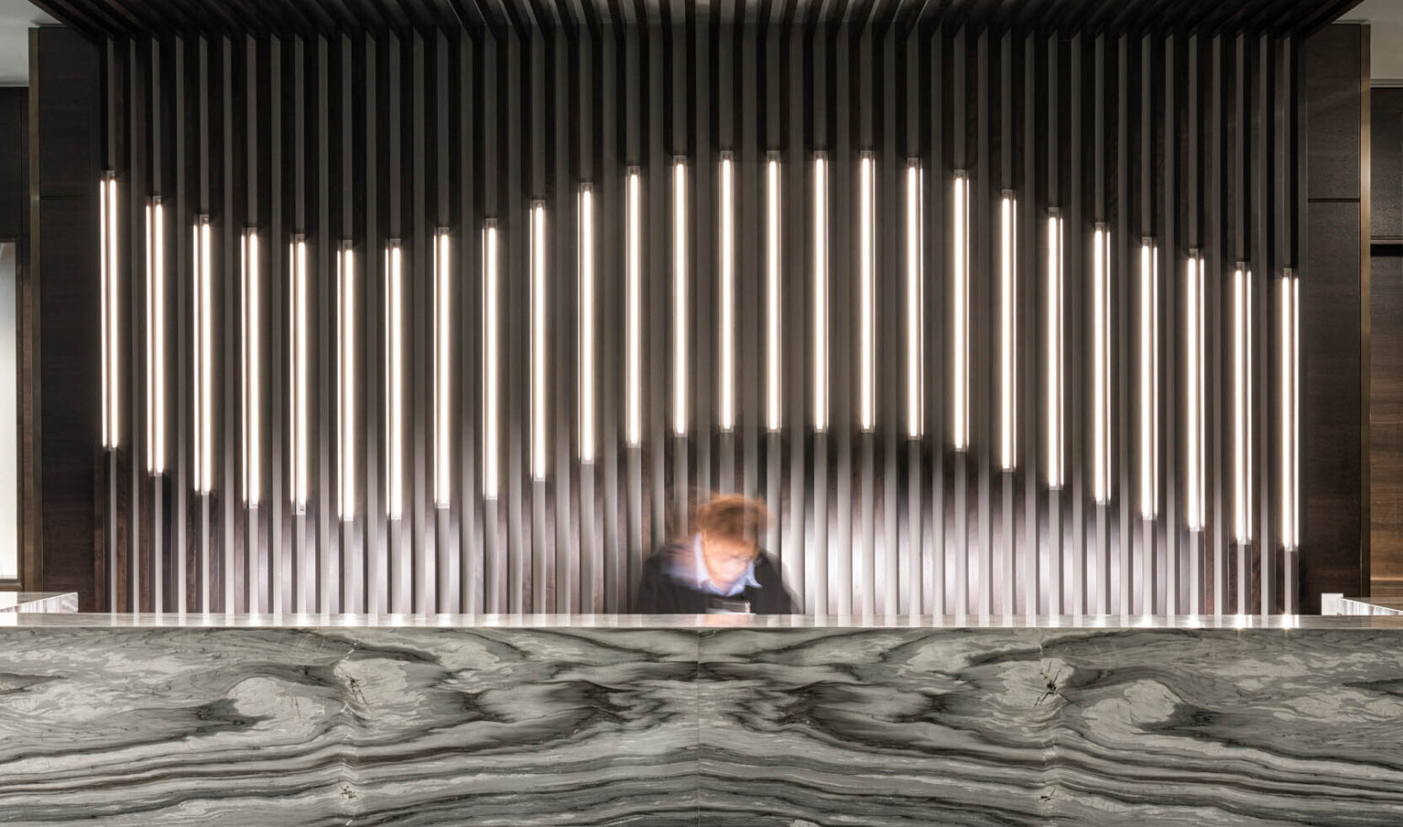 Dark marbled reception desk in lobby with thin pillared wall details, partially illuminated curve along center