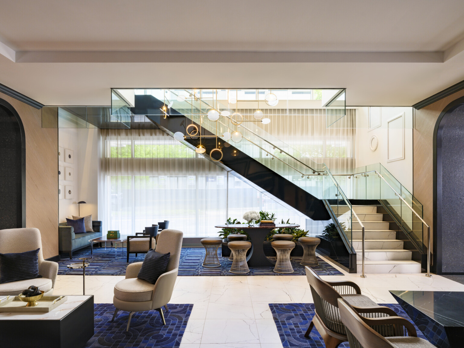 The Vanguard Hotel, Autograph Collection hotel lobby; tables and varied seating throughout the space; glass and black marble staircase separate room to room but open concept flows with natural and chandelier lights