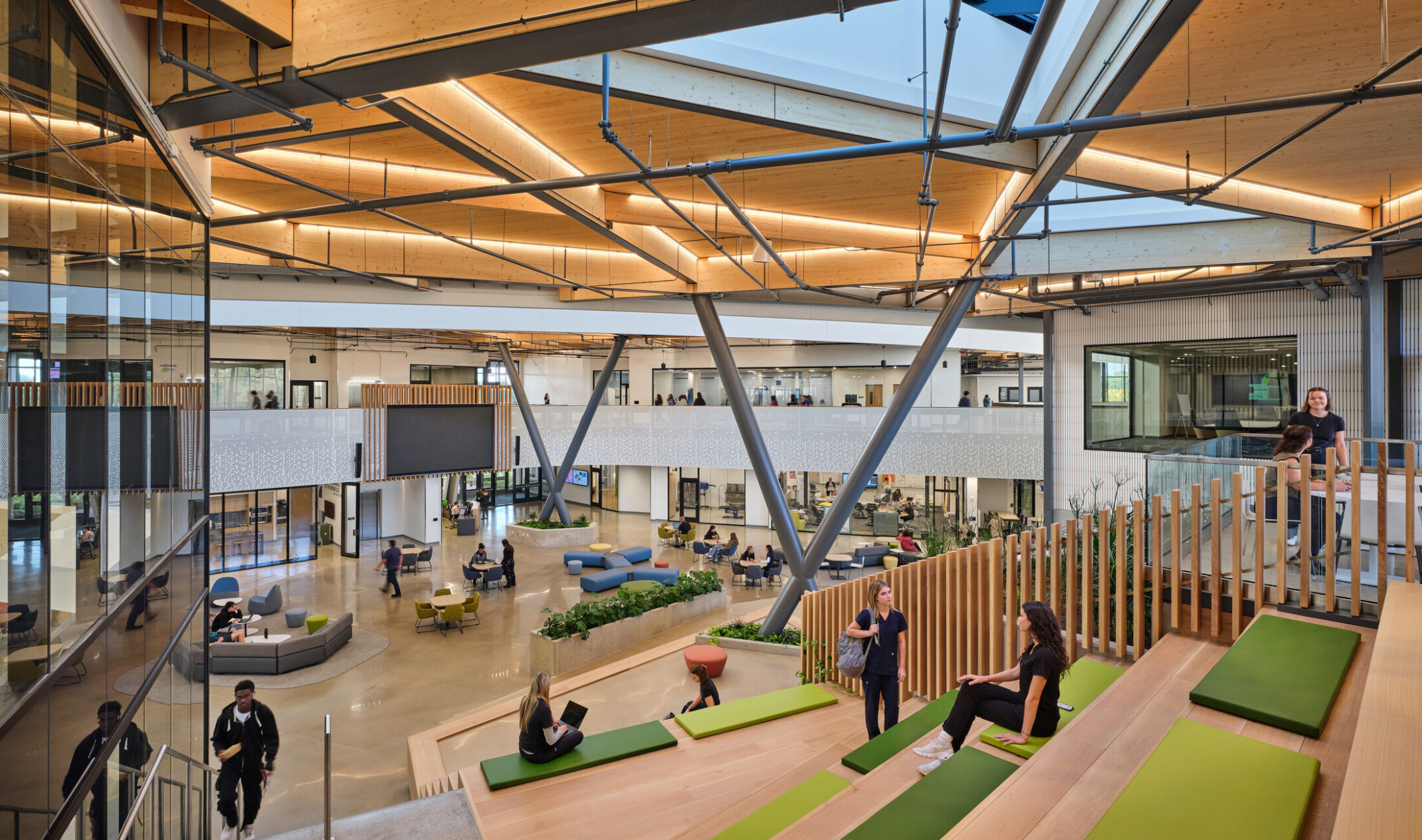 Kalamazoo RESA career technical education central open area featuring exposed wood structure, natural materials, and biophilic design elements; bleacher seating with green pads facing open space