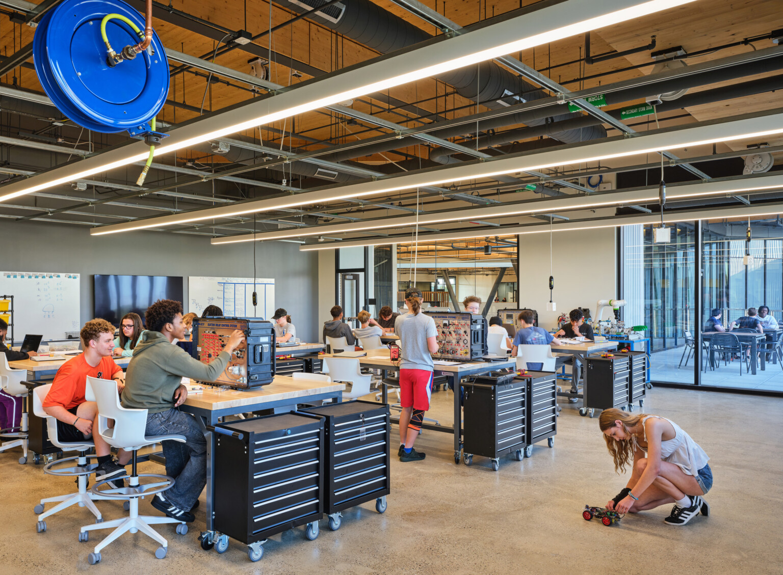 Industrial-style robotics classroom with exposed ceiling ductwork and students working at shop tables.