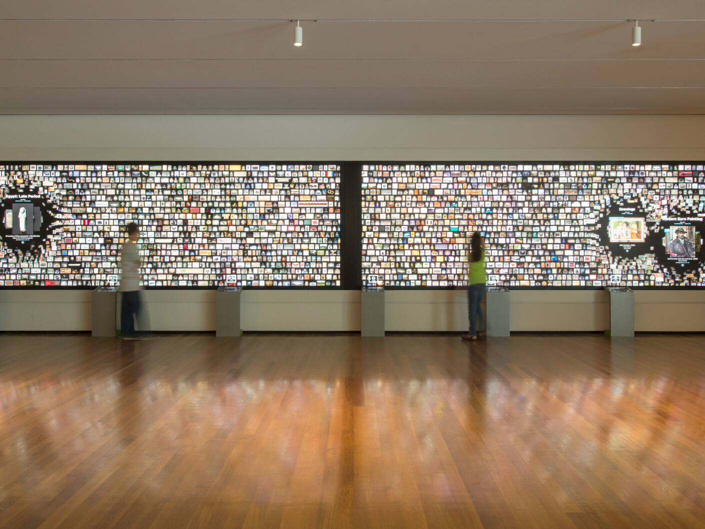 media exhibit in art museum comprised of two 8k screens combined displaying media, overhead spotlights maximize the focus on the screen, gleaming hardwood floors, high-ceilings, wide-open space