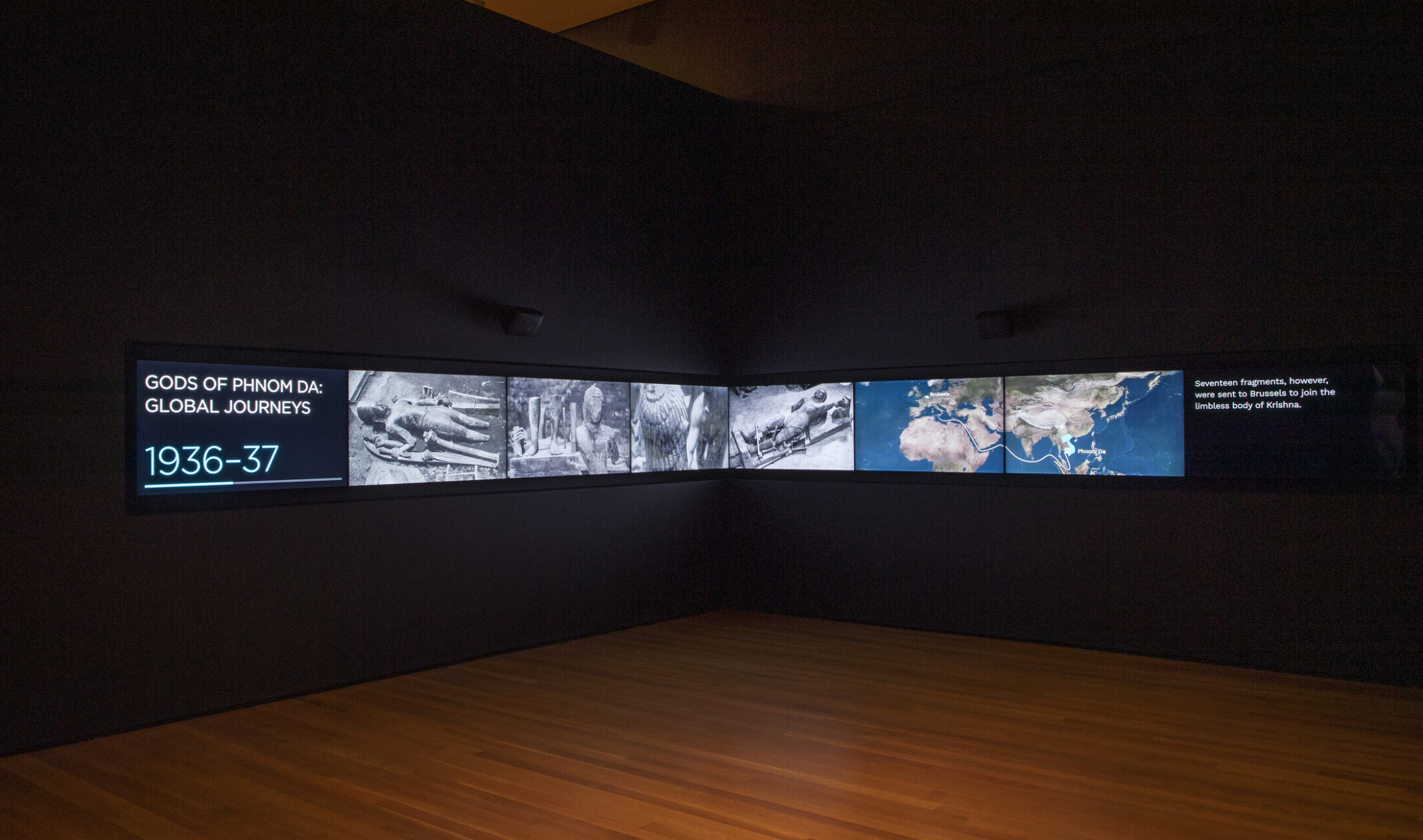 wood floor and two black walls with a timeline on large digital screens showing the journeys of the gods of phnom da 1936-37