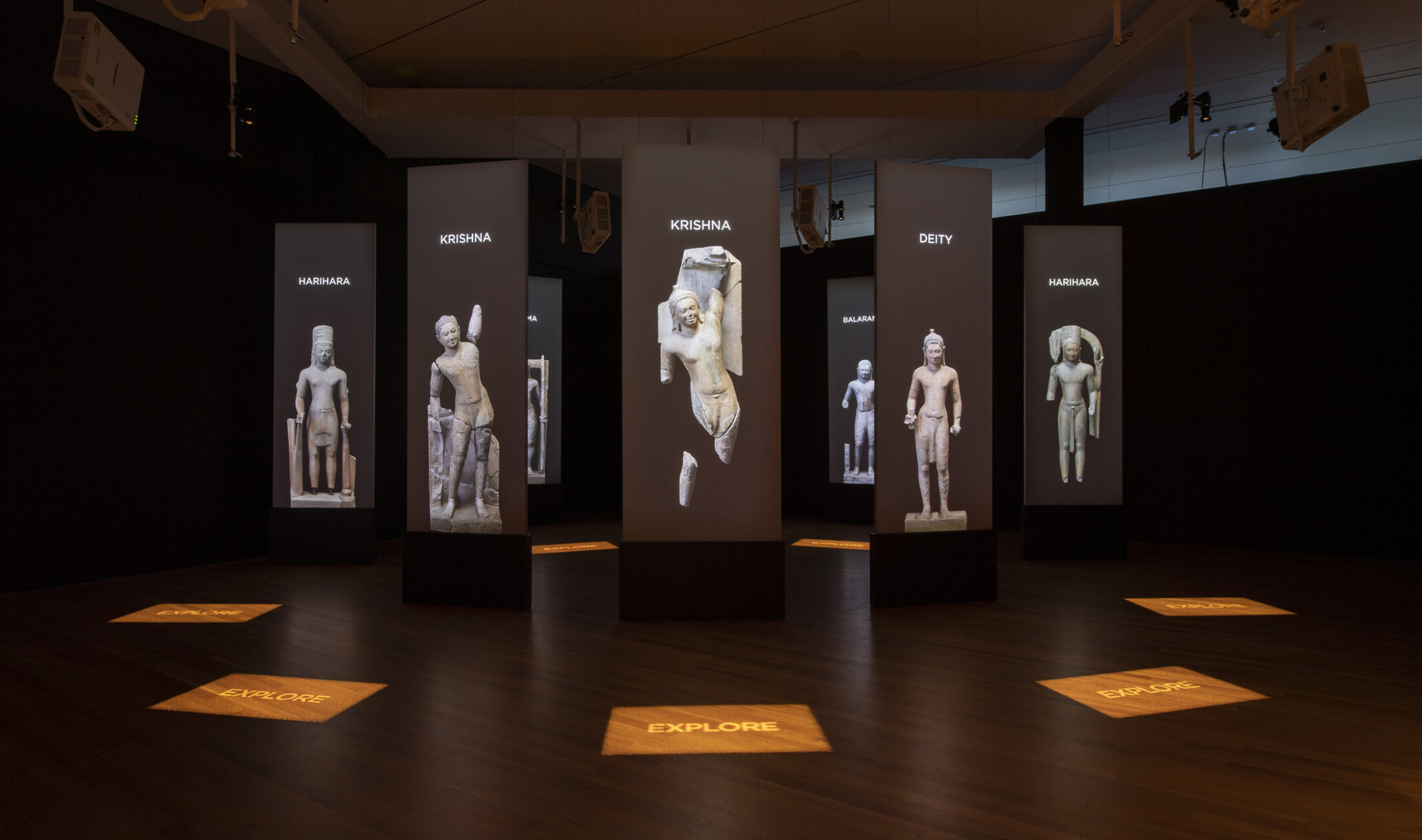 a darkened room with screens and stone statue images suspended in a circle pattern with illuminated signage on the wood floor