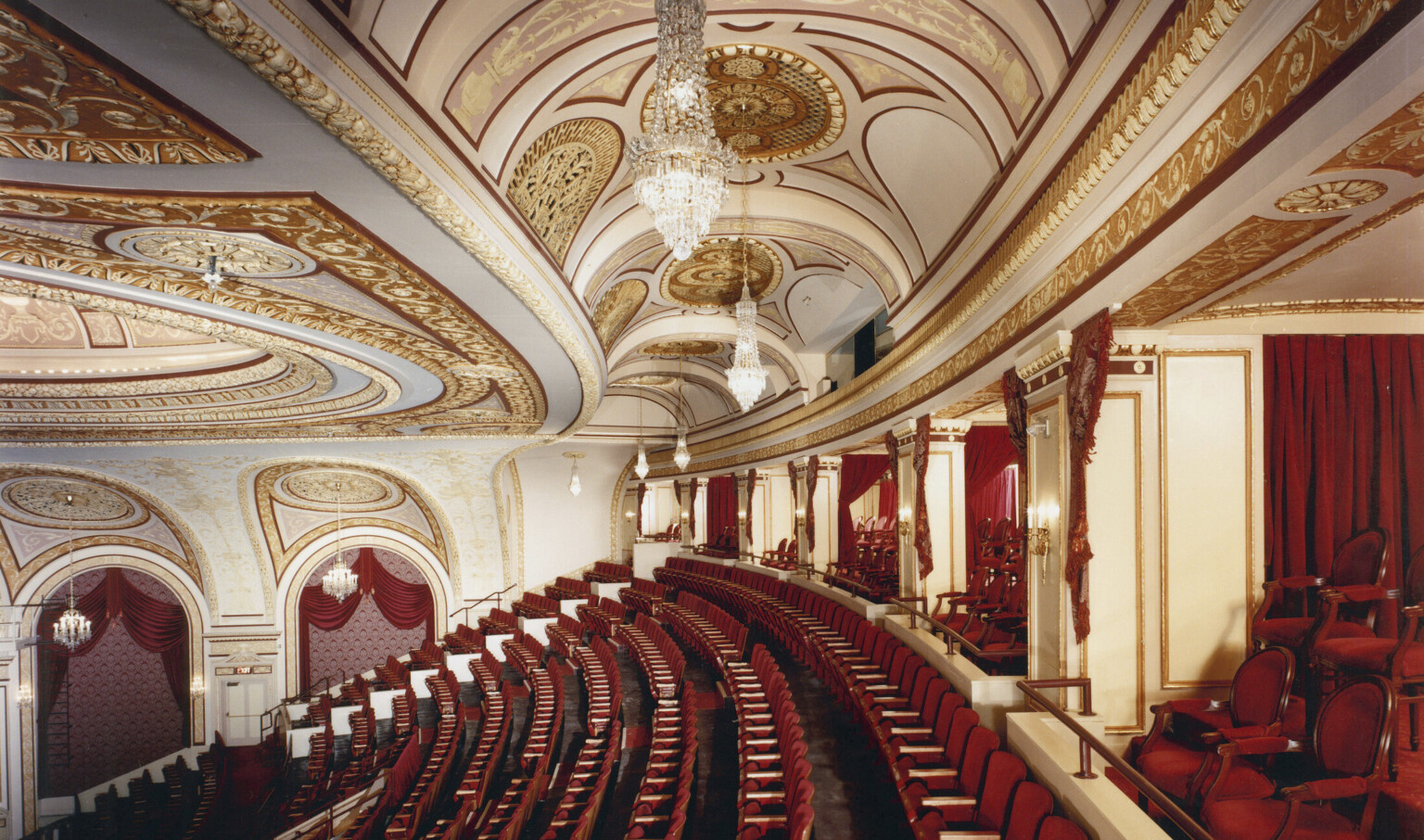 Box seats and back rows of audience in the Connor Palace Theater, with red seats and white walls with gold scroll details
