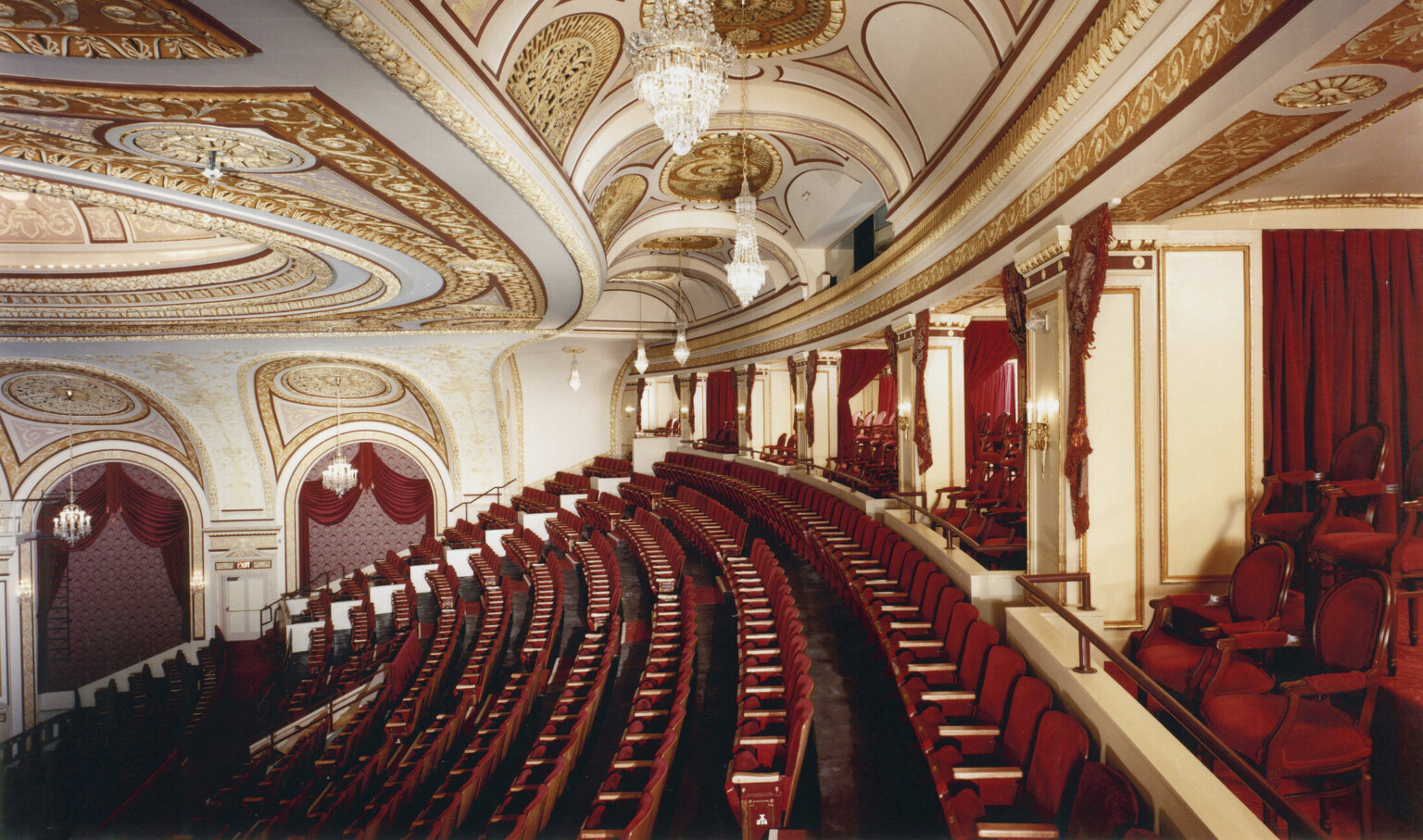 Box seats and back rows of audience in the Connor Palace Theater, with red seats and white walls with gold scroll details