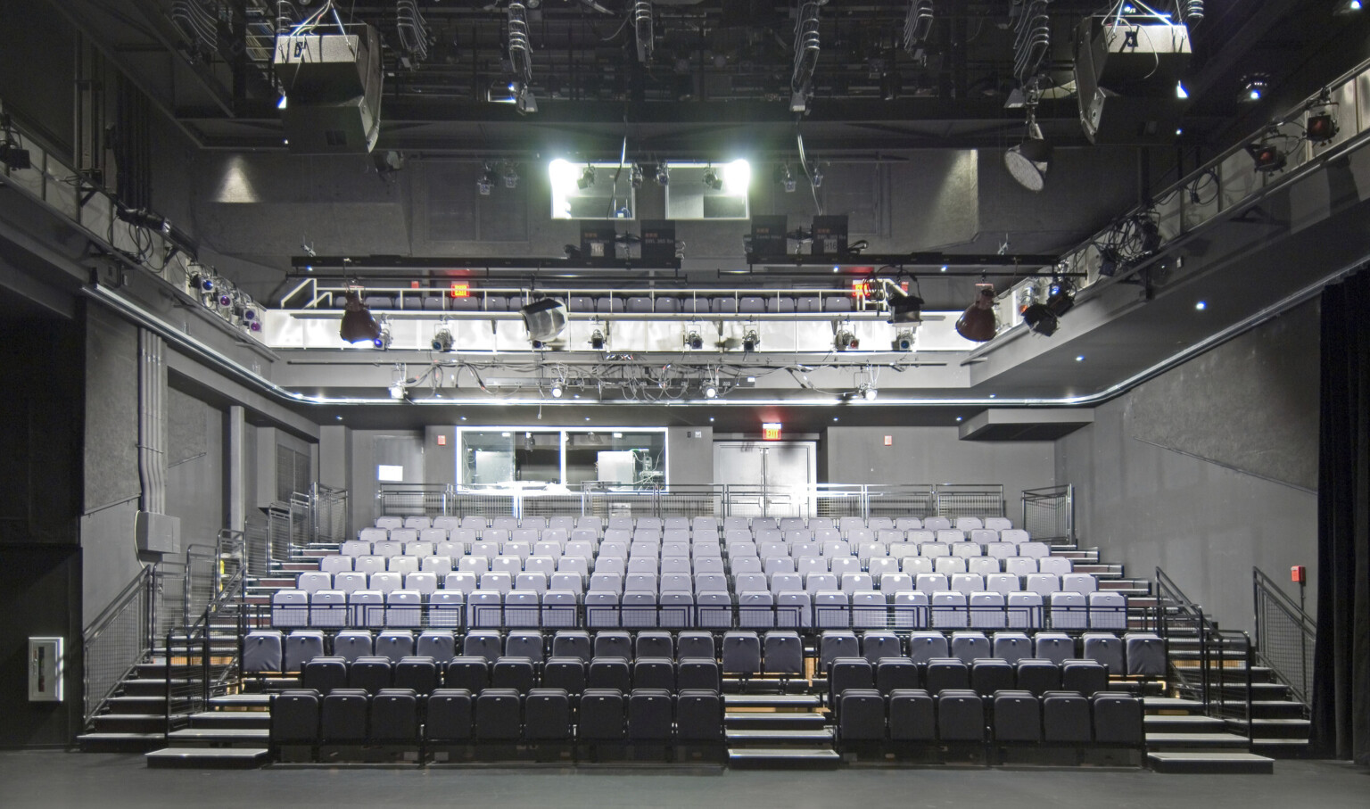 Two stories of stadium style grey seating in dark grey room with large light fixtures above