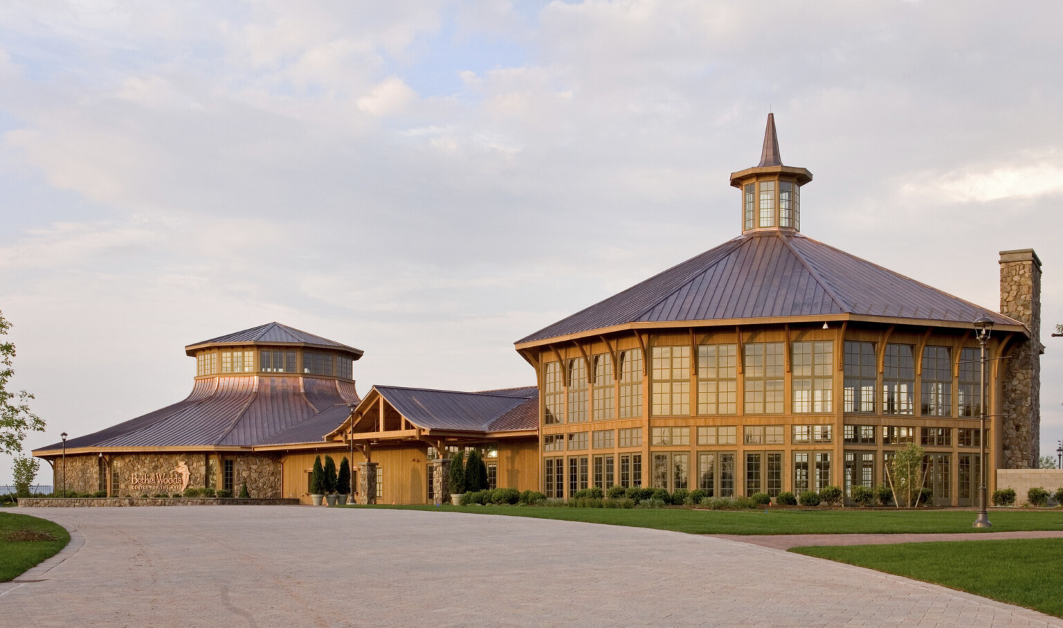 Rounded wood and window building with central spired cupola is connected by a single story entry to a round stone building