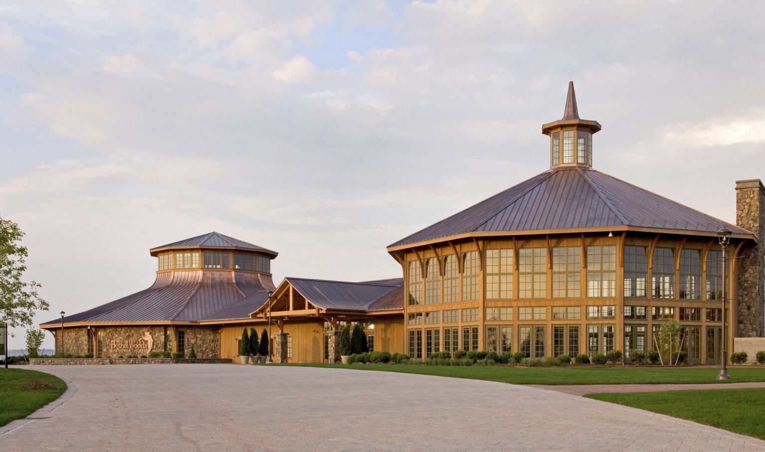 A large, rustic building complex filled with windows with copper roofs and extensive glass panels against a partly cloudy sky; Bethel Woods Center for the Arts