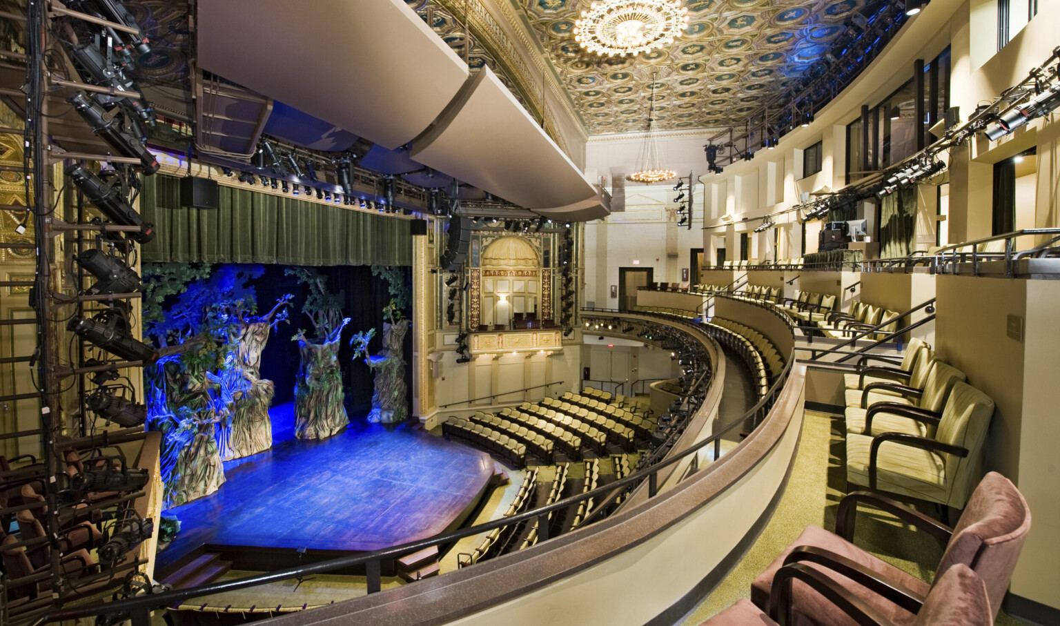 Multiple balconies in a theater with yellow seats and dark details, box seat center with arch overhang and gold details