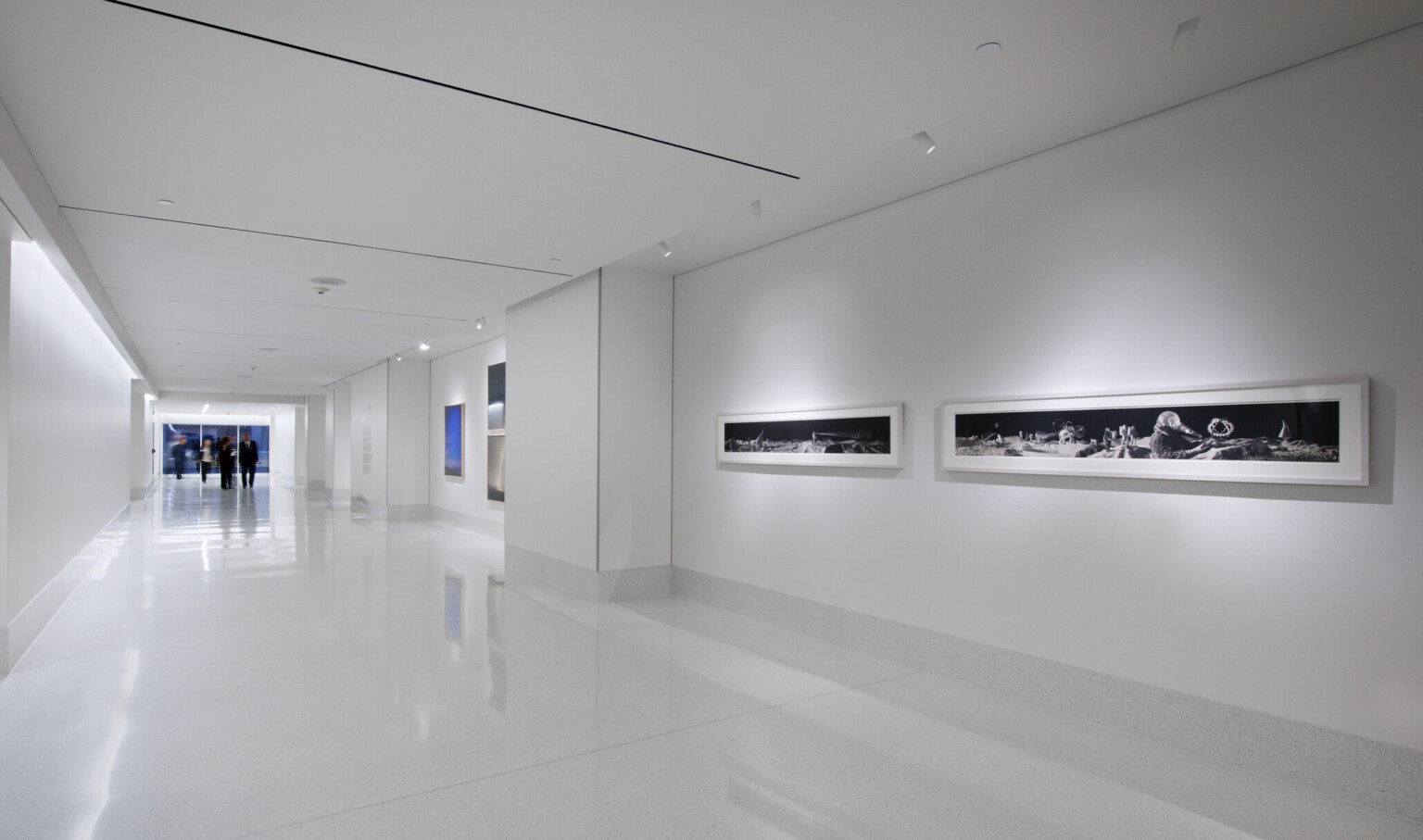 White hallway lit from above at the sides. Framed photographs line the right wall.