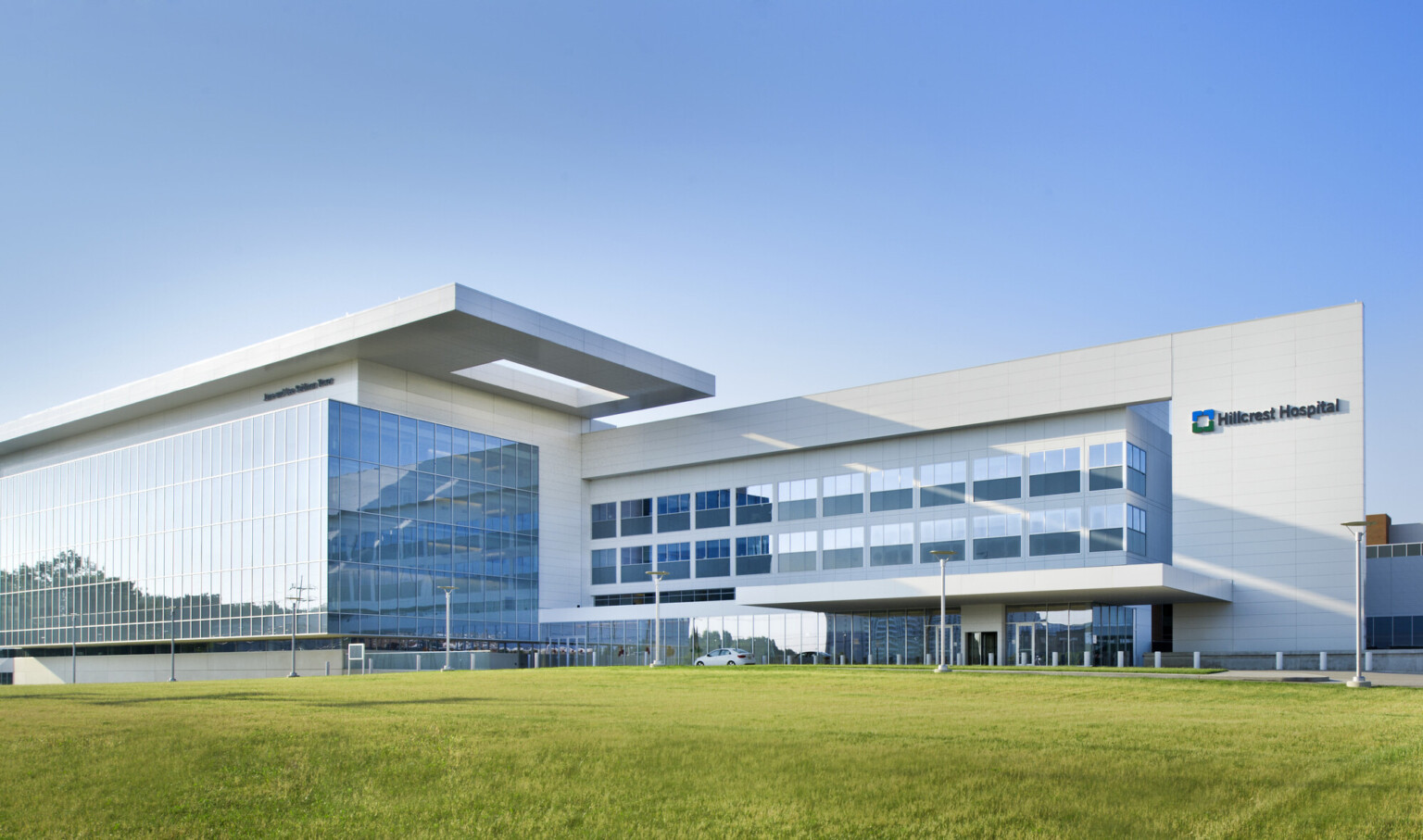Front of hospital viewed from across the grass. Multistory windowed outcrop wraps around left section with overhang above