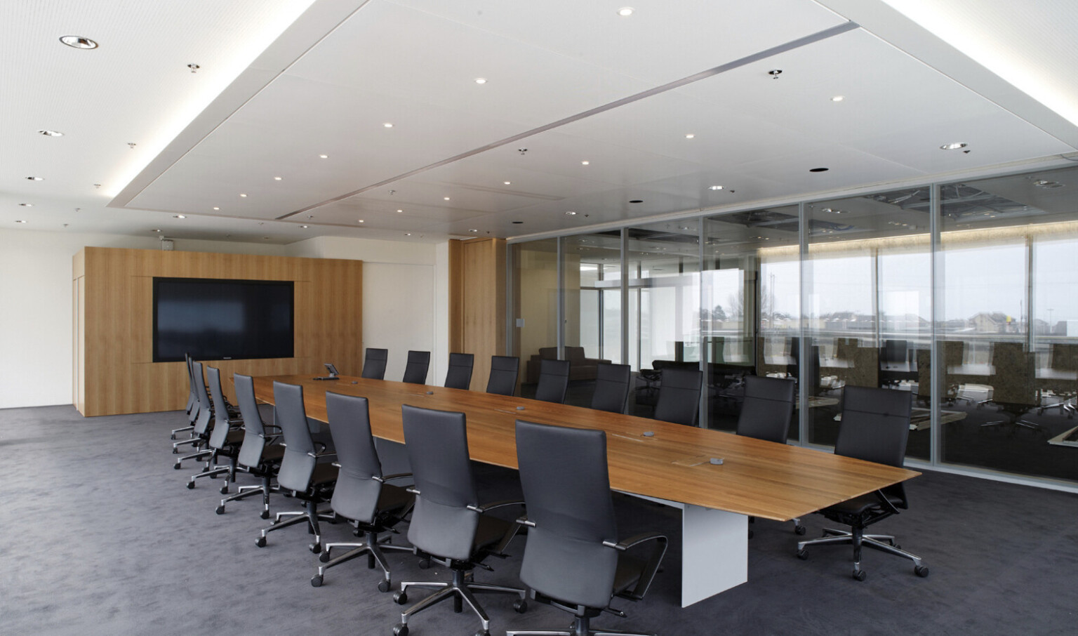Conference room with long wood table and chairs across from wood accent wall with screen. Interior floor to ceiling windows