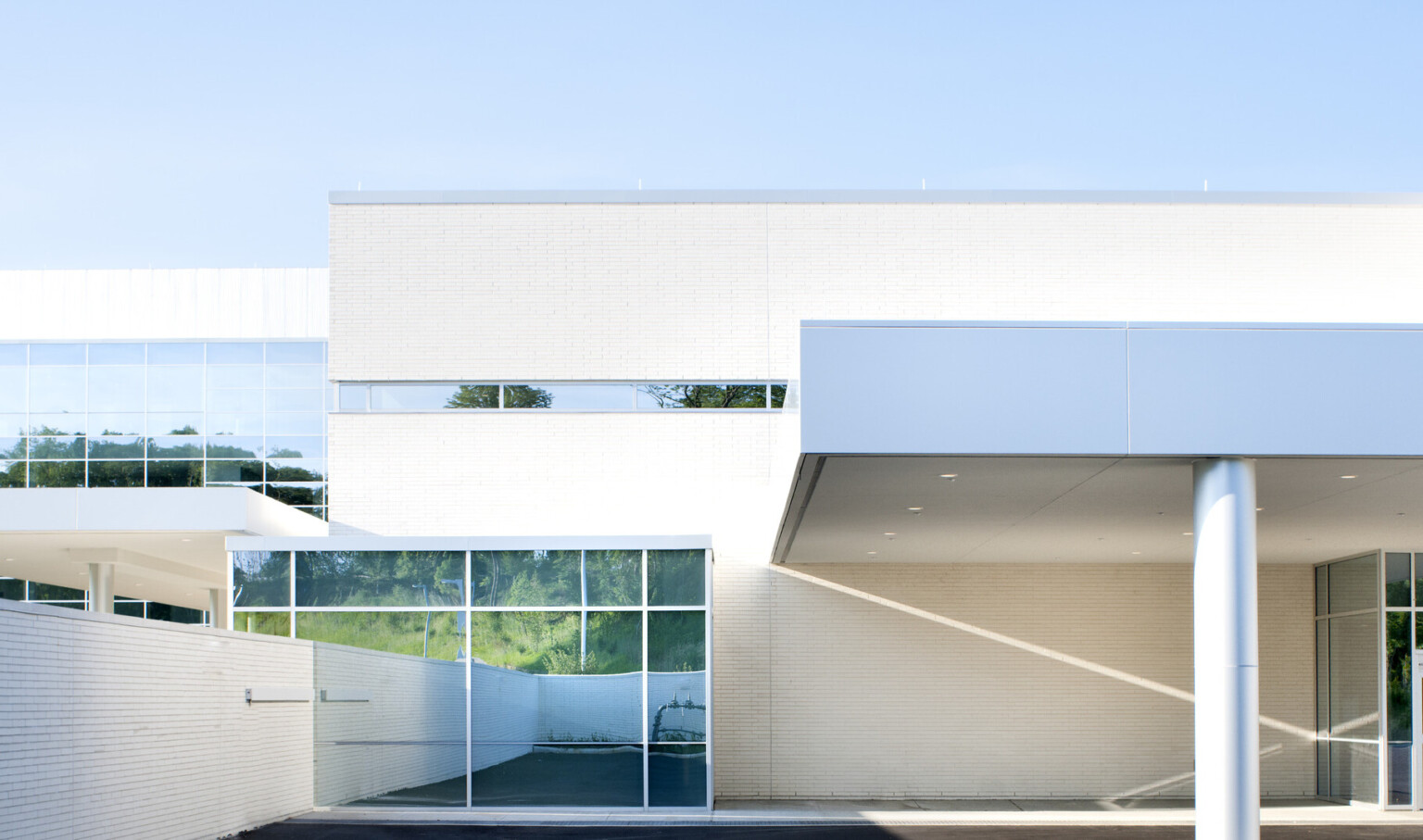 White stone building. Outcrop with floor to ceiling windows left with stone wall. Grey metal pillar with overhang right