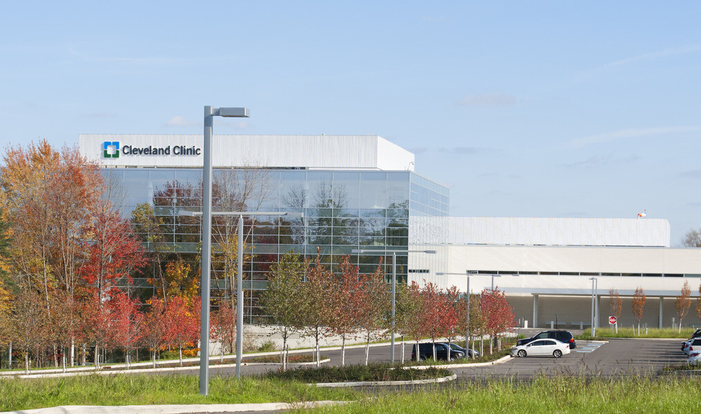 View of white and glass building from grass across the parking lot. Sign over glass building section reads Cleveland Clinic