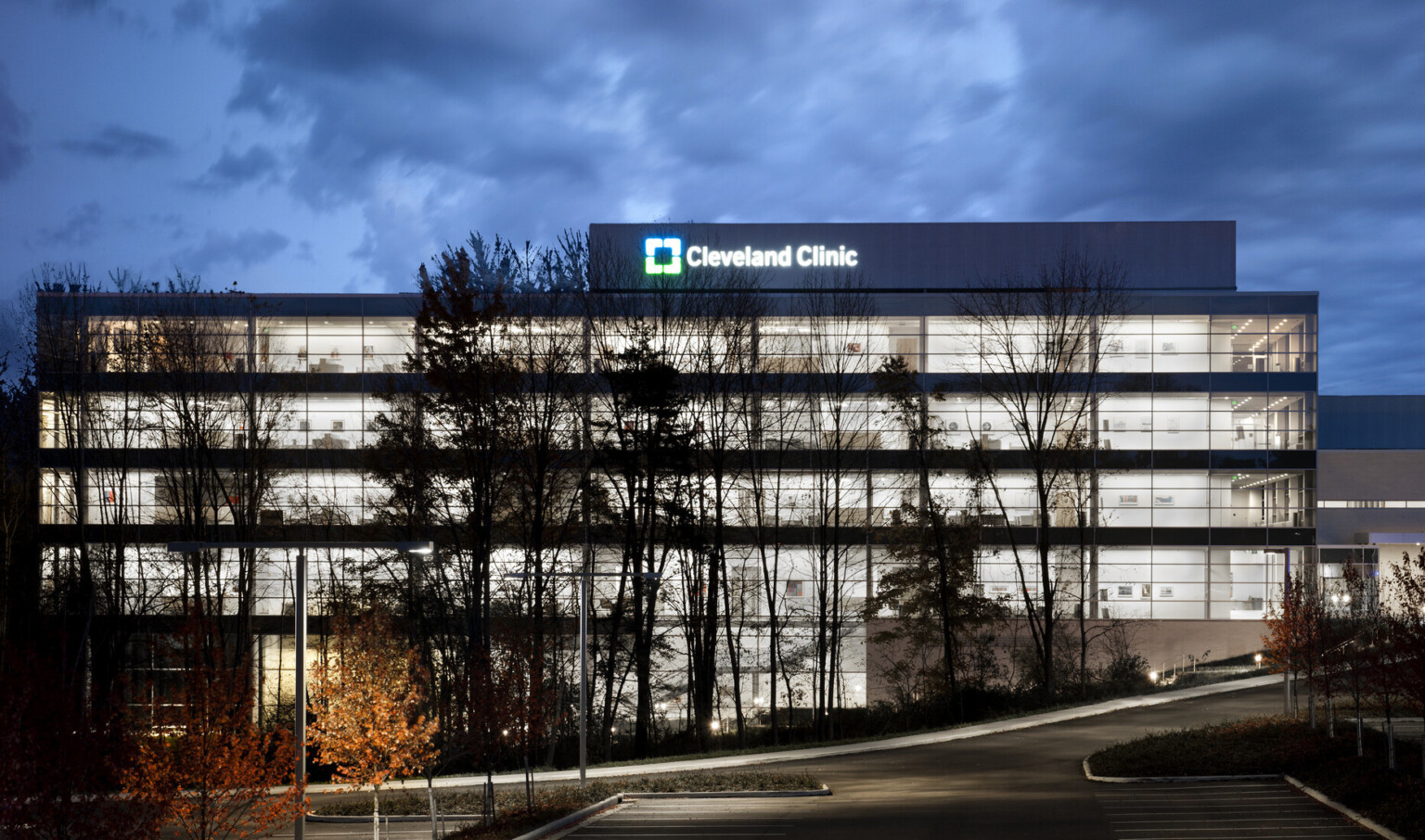Exterior view of building illuminated at night with bottom floor built into hill. Lit sign at top reads Cleveland Clinic