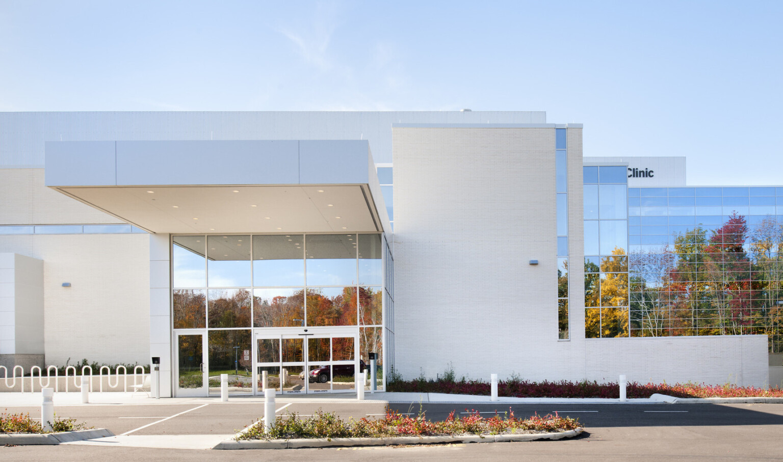 Entry with double height windows with white overhang extending over driveway. White wall right with window wall beyond