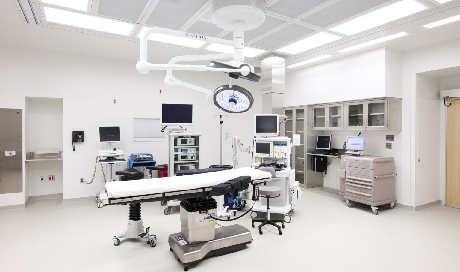 Operating room with bed center, movable lights hang from above. Stool at head next to portable screens and equipment