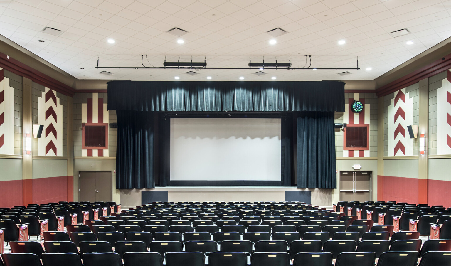 Theater with red band on wall below geometric red and white tiles. Dark blue curtains around screen match with seat backs