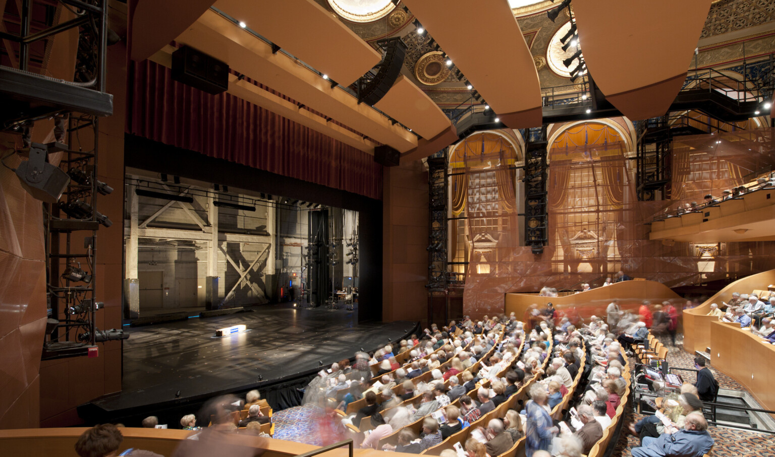 Theater seen from the side over the audience with large arch shaped windows. The stage is empty and stage right can be seen