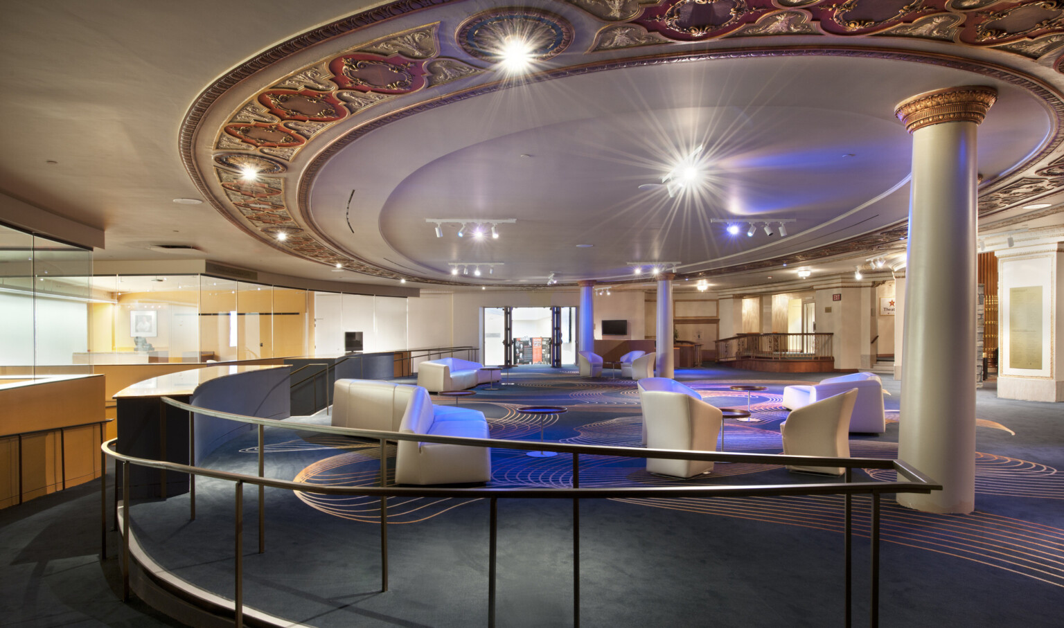 Lobby with dark colored carpet with gold organic design. White angled seats through out the room below a round ceiling detail