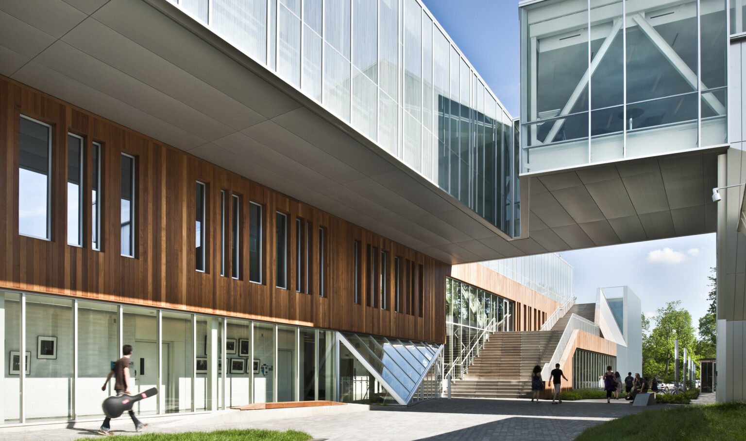 Partially covered walkway between buildings, building at left has first floor window walls below wood panels