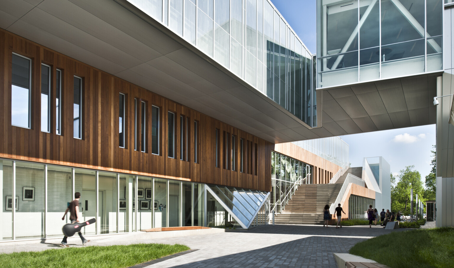 Partially covered walkway between buildings, building at left has first floor window walls below wood panels