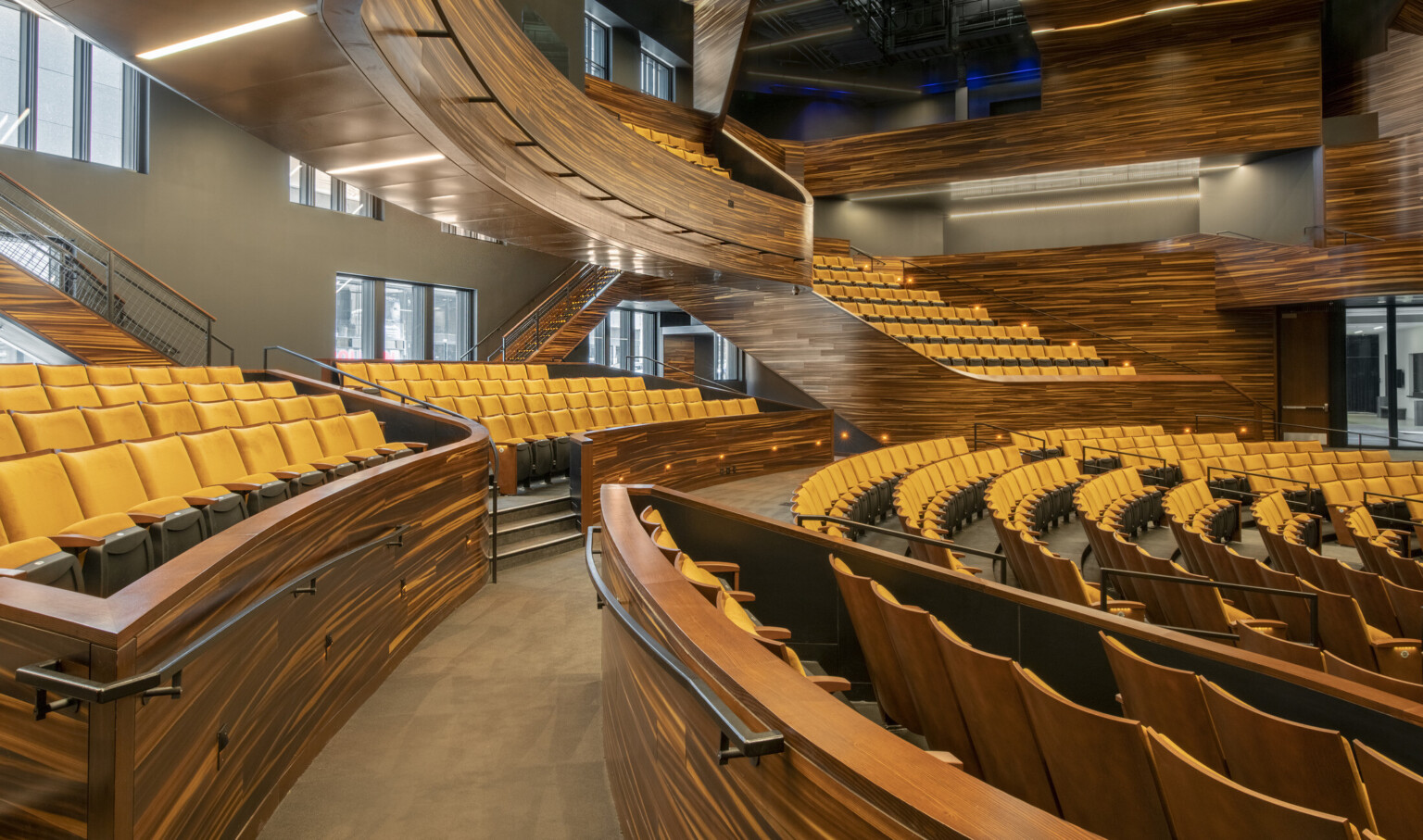 Stadium style yellow seating and abstract stripe stained wood details, balcony, and bannisters with recessed aisle lighting