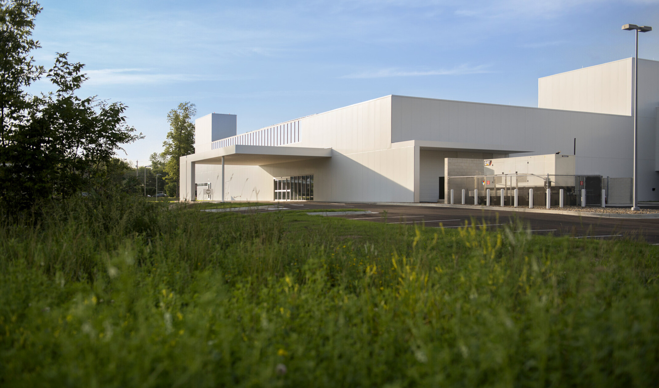 grass and trees in foreground of white modern angular building side entrance with sliding glass doors covered by white canopy