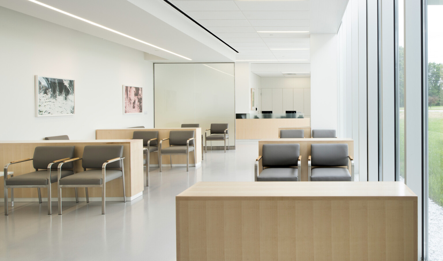 White room with seating area separated from wood reception desk by translucent glass. Wood dividers between seating sections