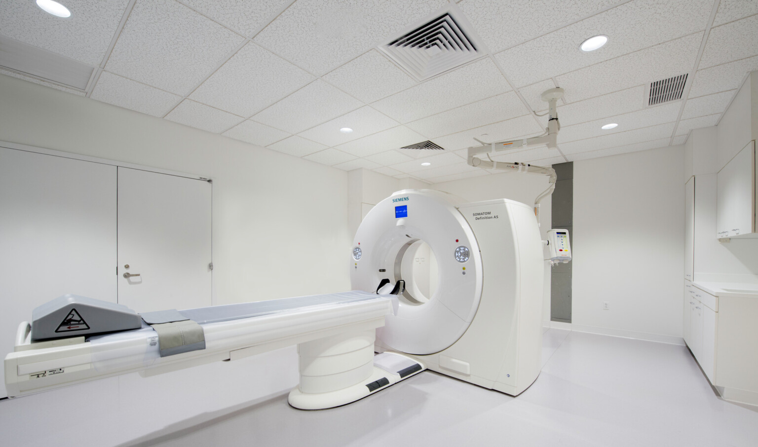 MRI machine at center of white room viewed from the corner near the foot