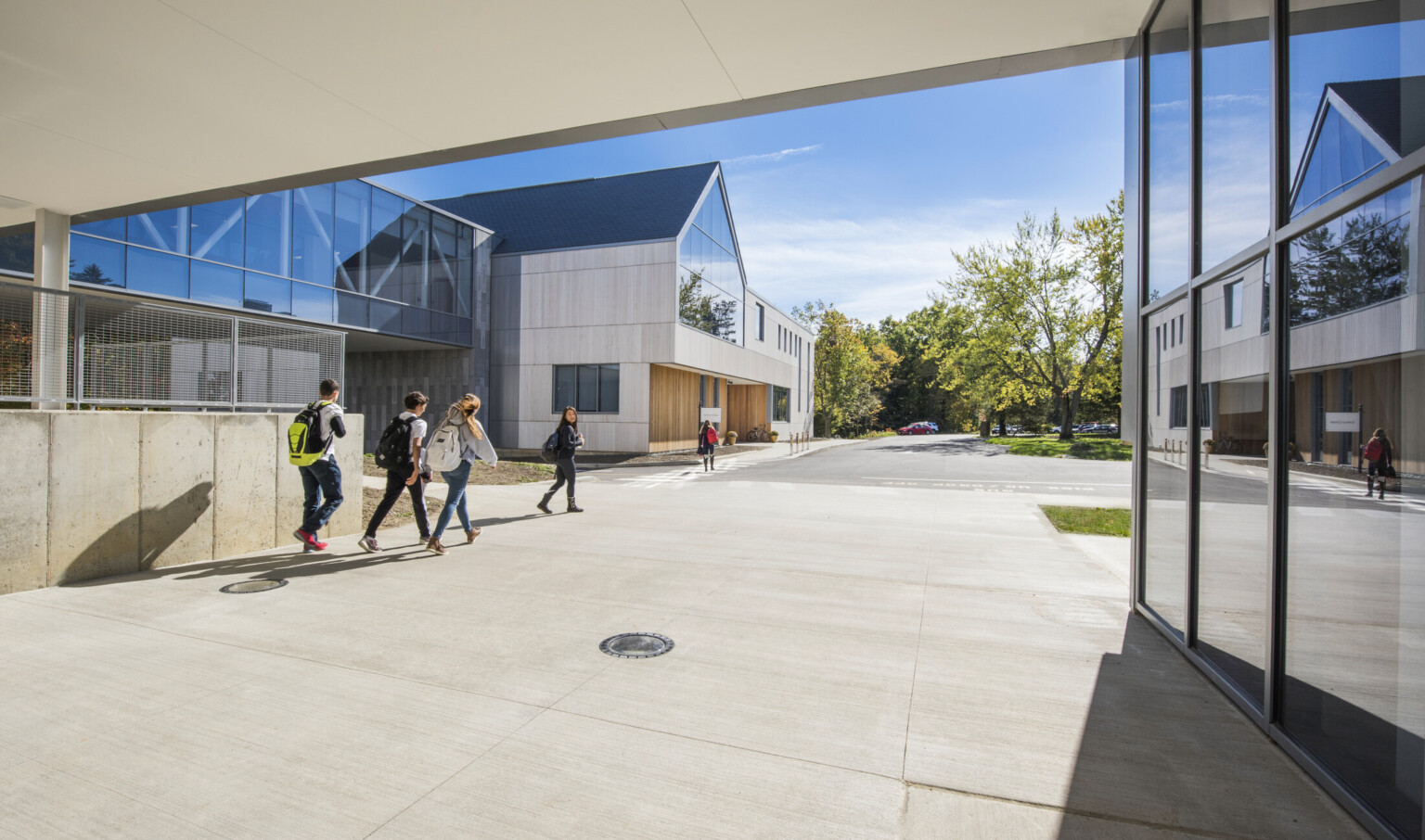 Exterior covered walkway between 2 buildings. Floor to ceiling windows, right. Left, an elevated hallway to stone building