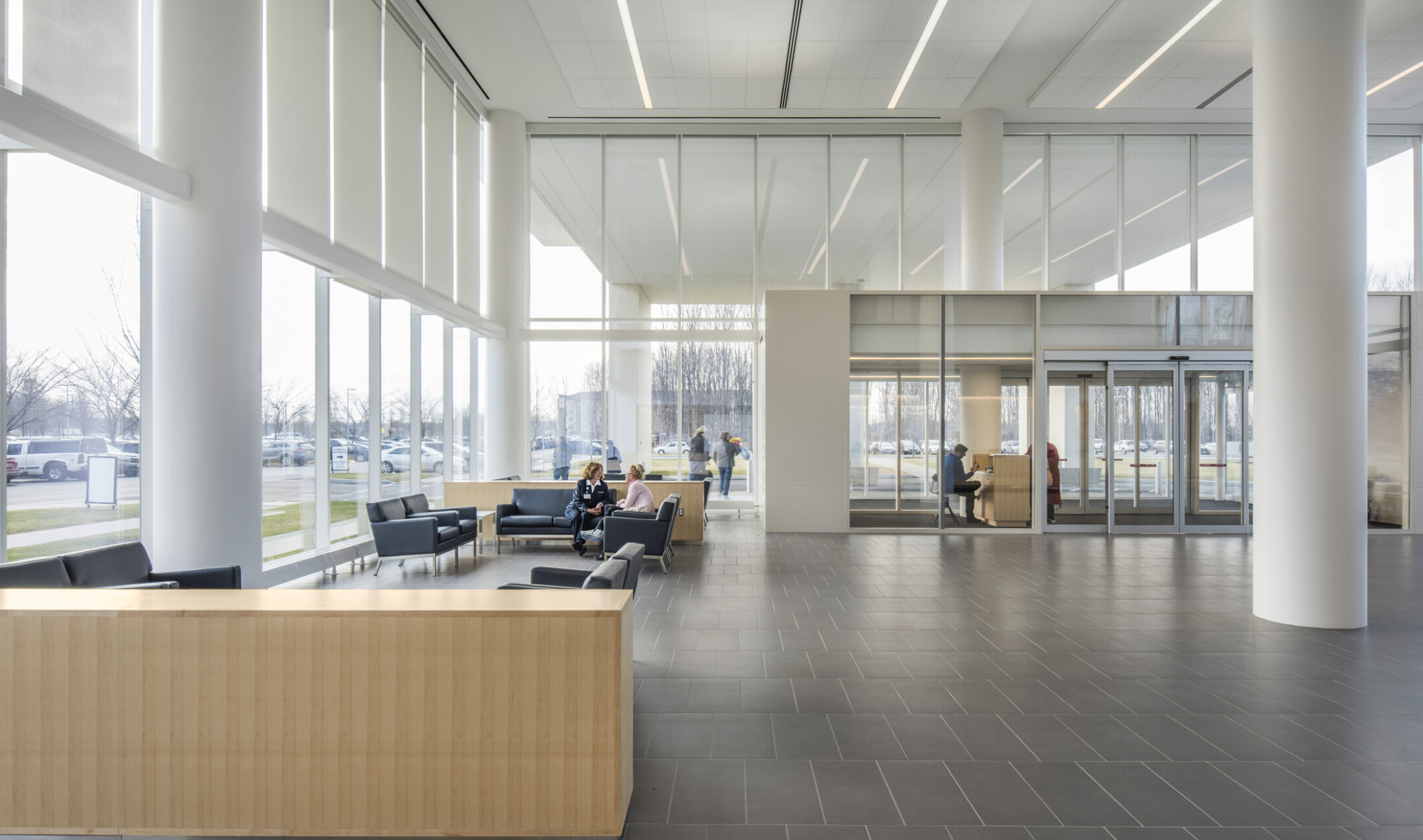 Lobby with double height windows and glass antechamber. Seating area is to the left with couches in a white room with pillars