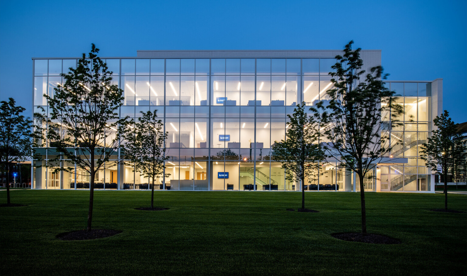 Side of building at night, illuminated so all 3 floors are visible through the floor to ceiling windows