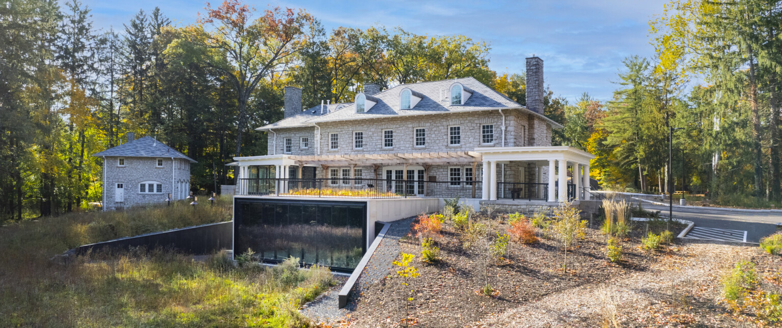 Stone façade mansion nestled in lush, tall trees, greenery, blue skies