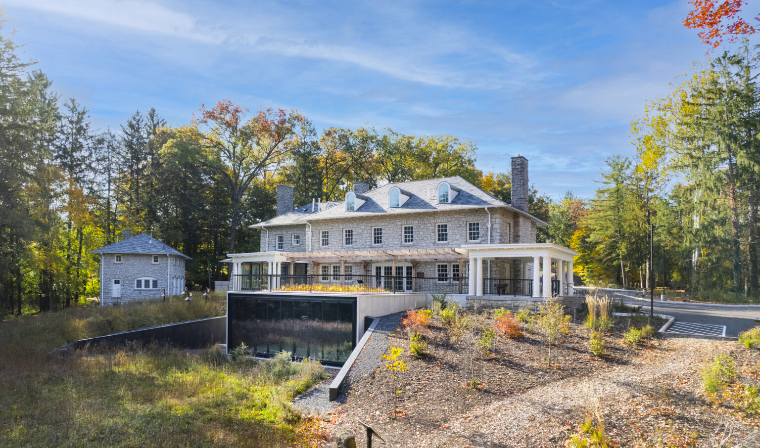 Stone façade mansion nestled in lush, tall trees, greenery, blue skies