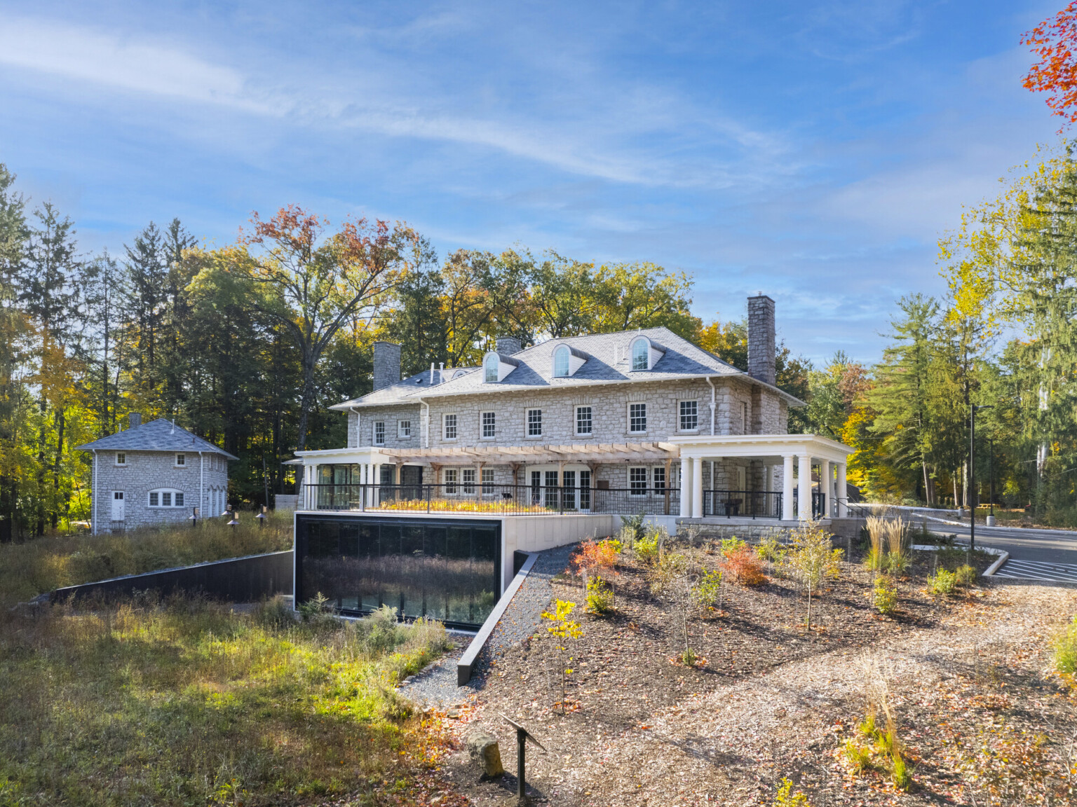 Stone façade mansion nestled in lush, tall trees, greenery, blue skies