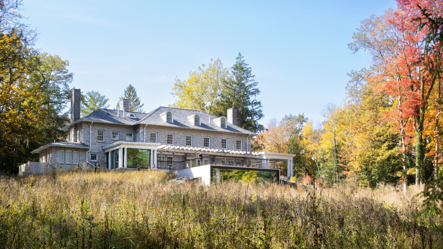 Mill Creek MetroParks Ford Nature Center a stone façade mansion nestled in lush, tall trees, greenery, blue skies