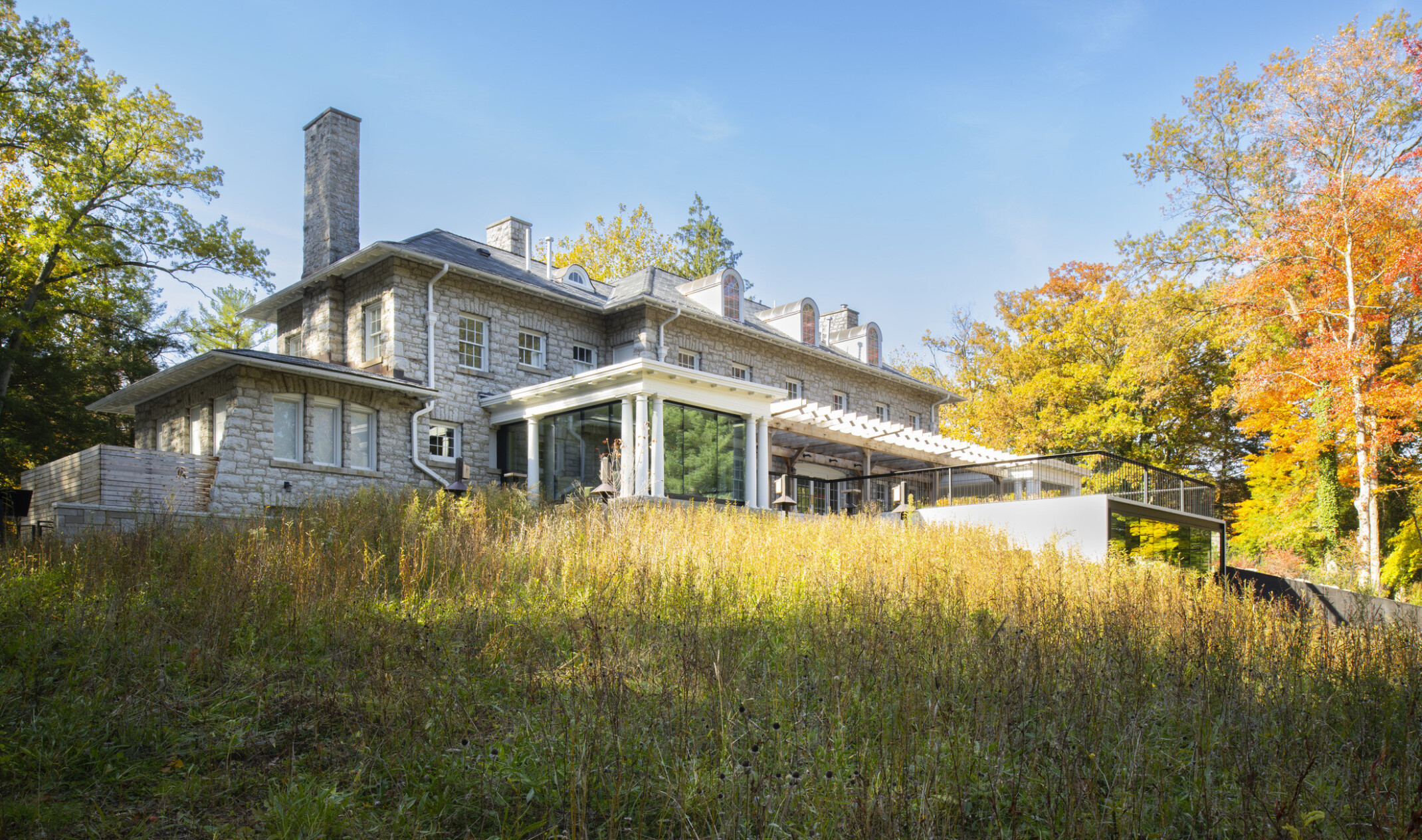Stone façade mansion nestled in lush, tall trees, greenery, blue skies