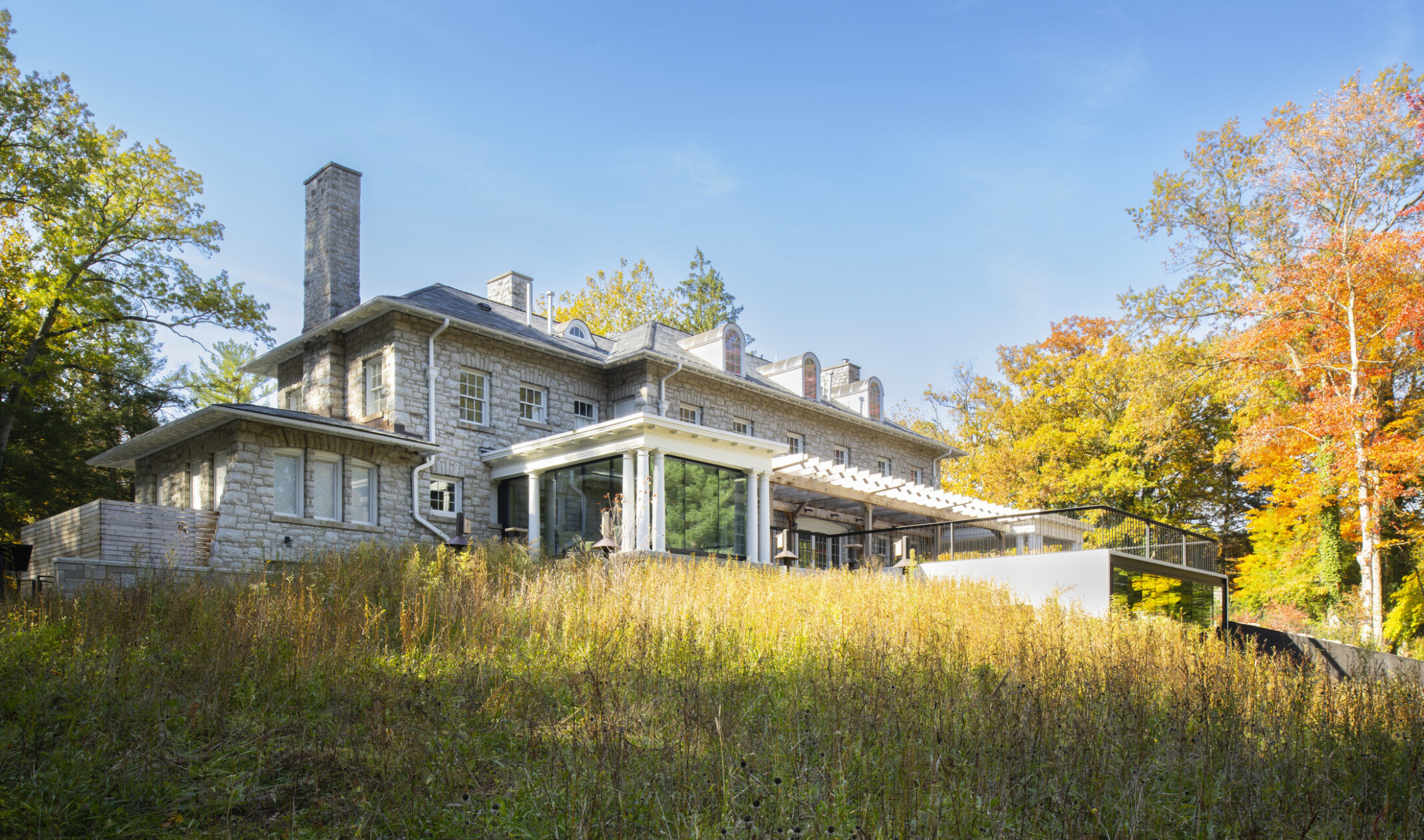 Stone façade mansion nestled in lush, tall trees, greenery, blue skies