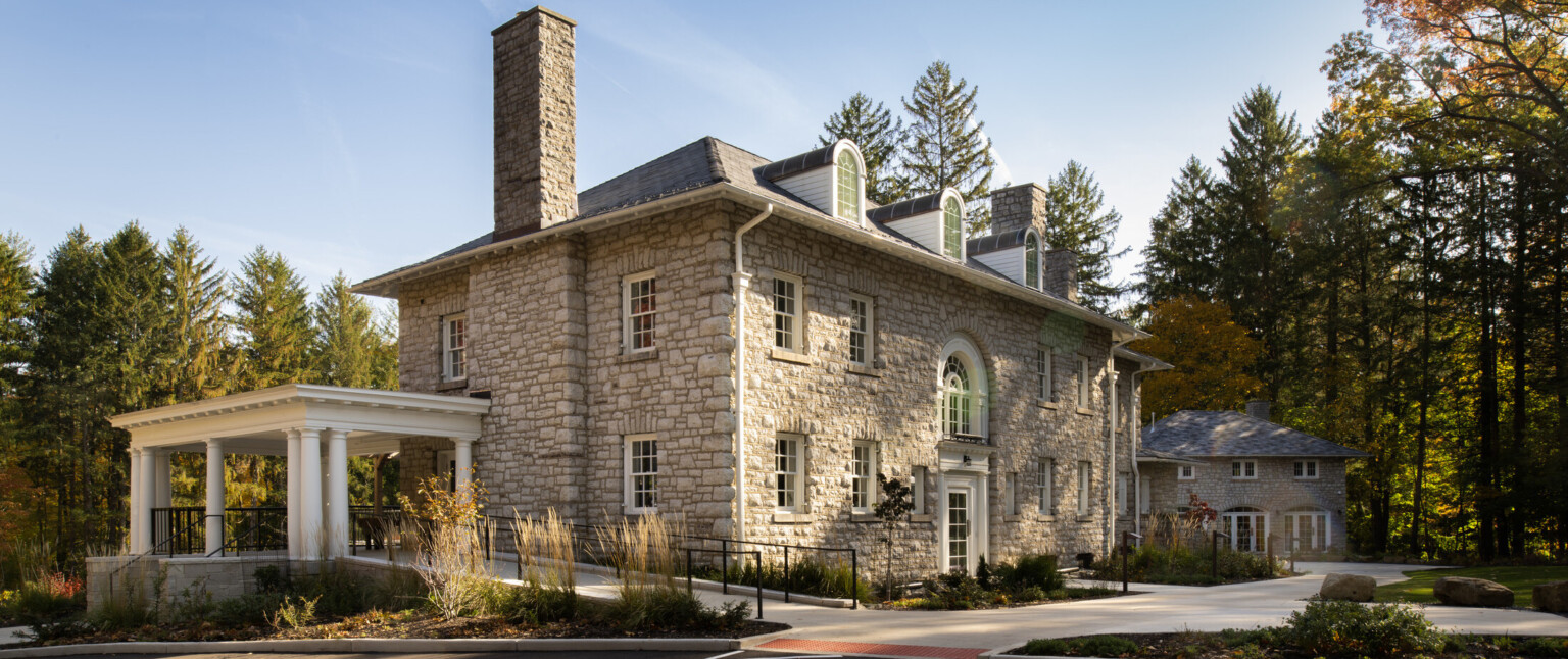 Stone mansion building nestled in lush, tall trees, greenery, blue skies