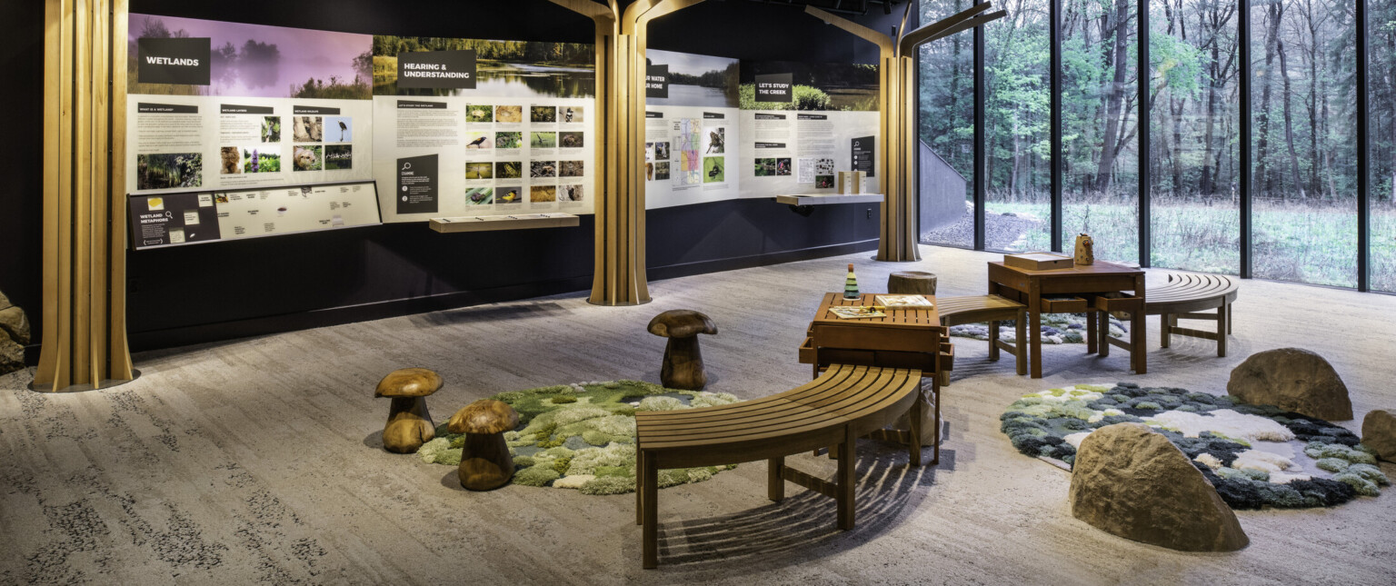 Classroom with wooden tree sculptures with wooden benches and large glass windows overlooking lush greenery