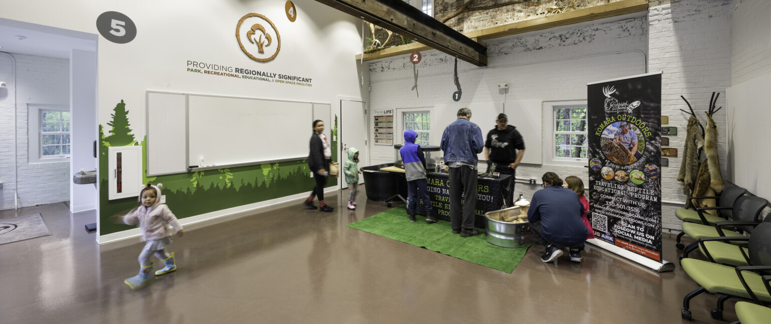 People interacting in a brightly lit room with green chairs, brown floors, and trees painted on the walls People interacting in a brightly lit room with green chairs, brown floors, and trees painted on the walls