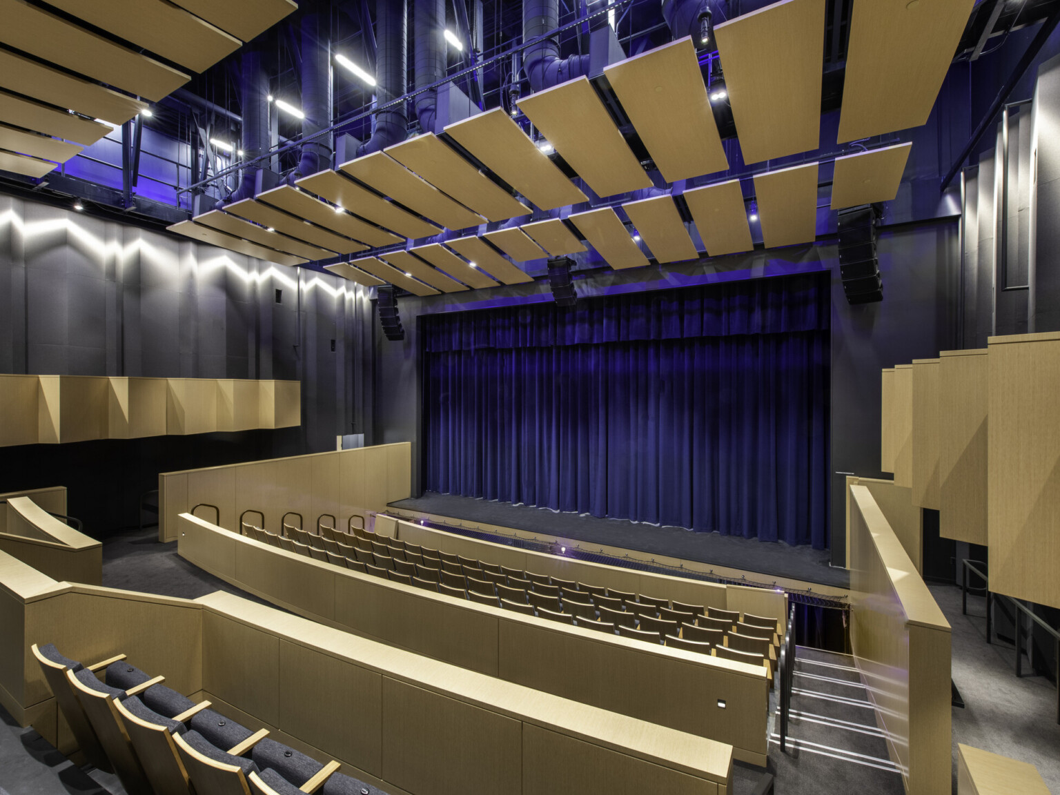Theater with wood panels on black walls and ceiling matching seat backs.