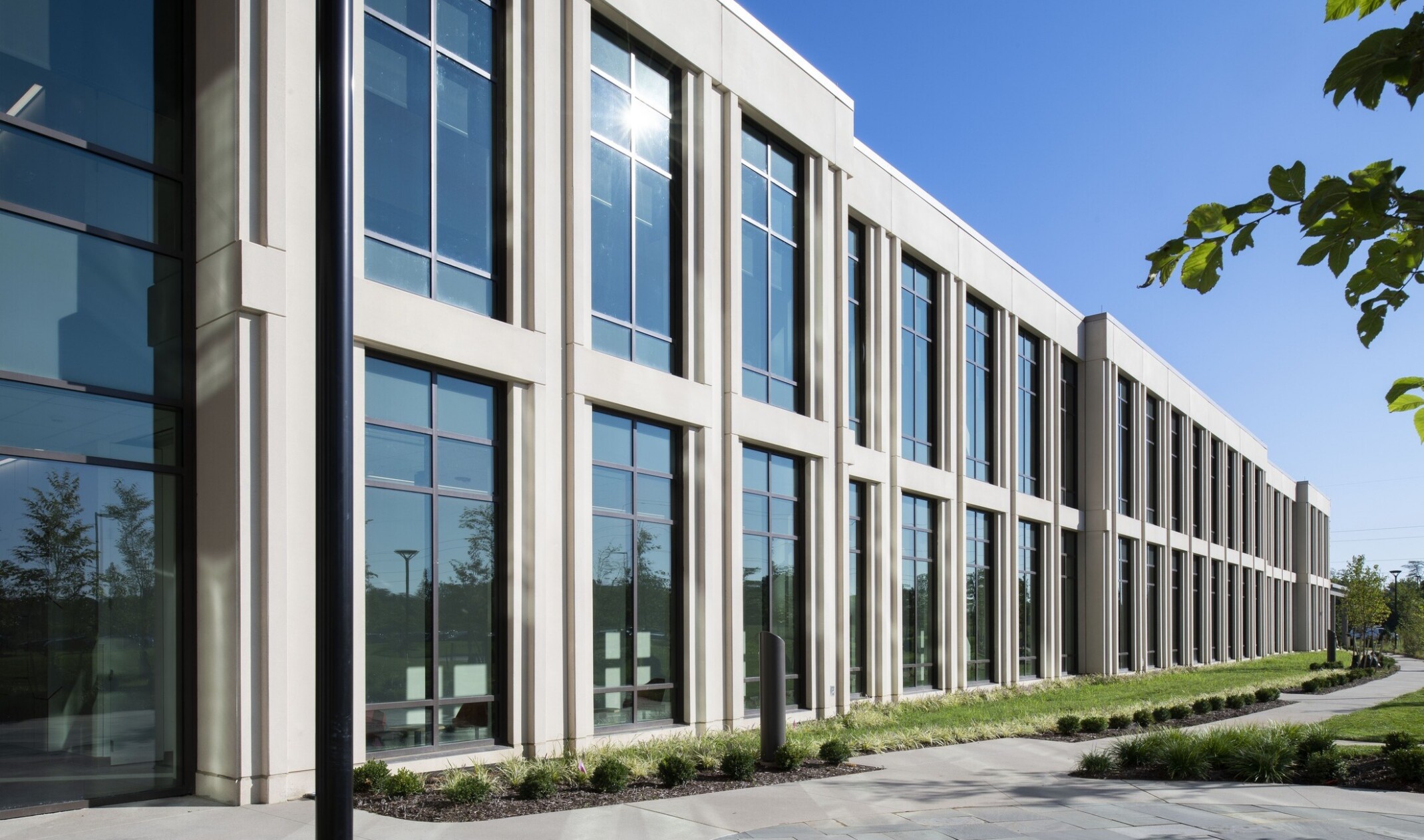 exterior of side view of a modern building with cement framing with large windows; foreground sidewalk with greenspace