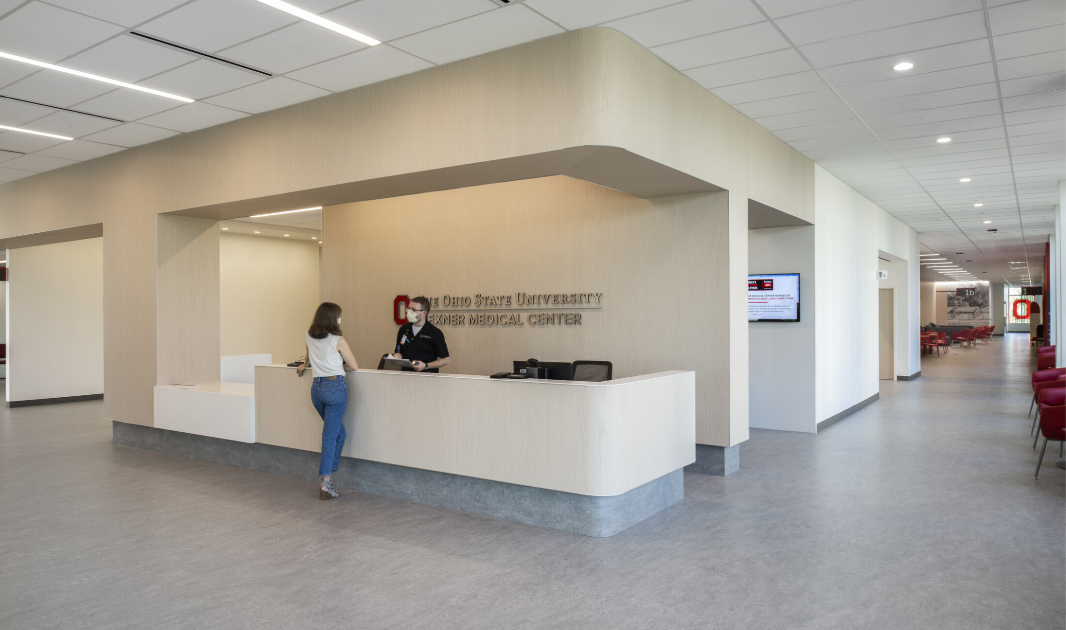 Entry reception desk in medical center. Beige desk matches wall colors, grey base matches floors. White panel ceiling