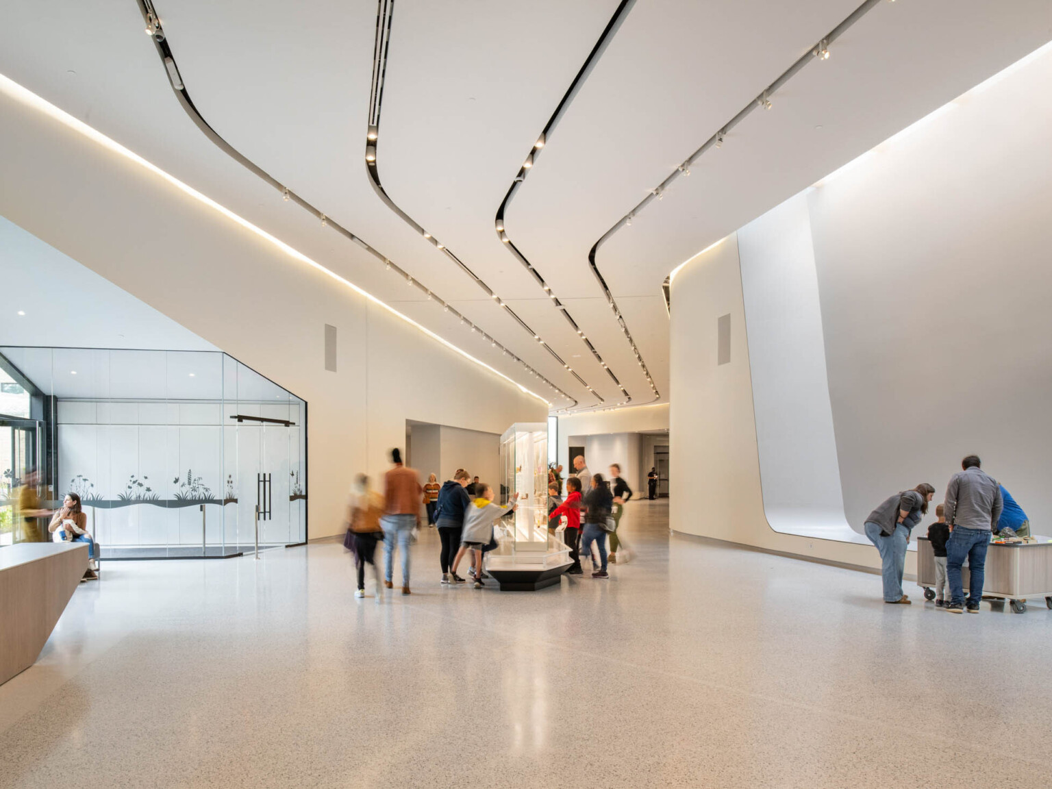 Museum gallery filled with people with white walls and large glass area