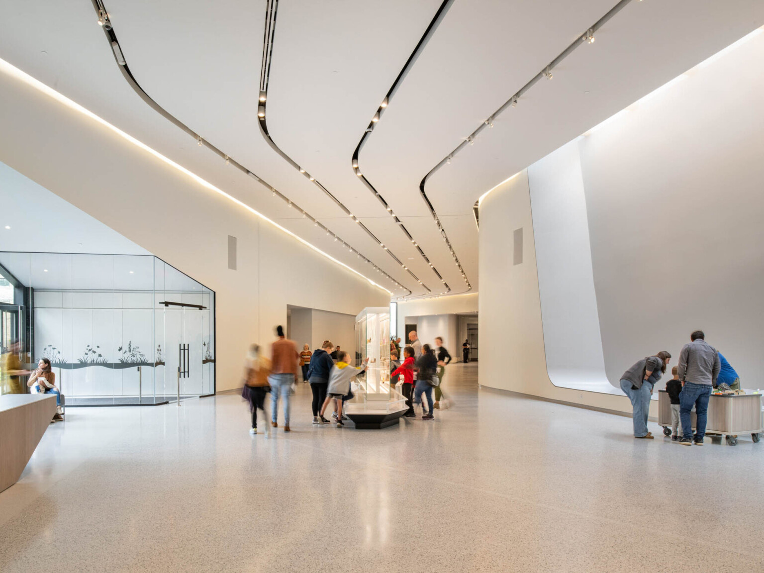 Museum gallery filled with people with white walls and large glass area