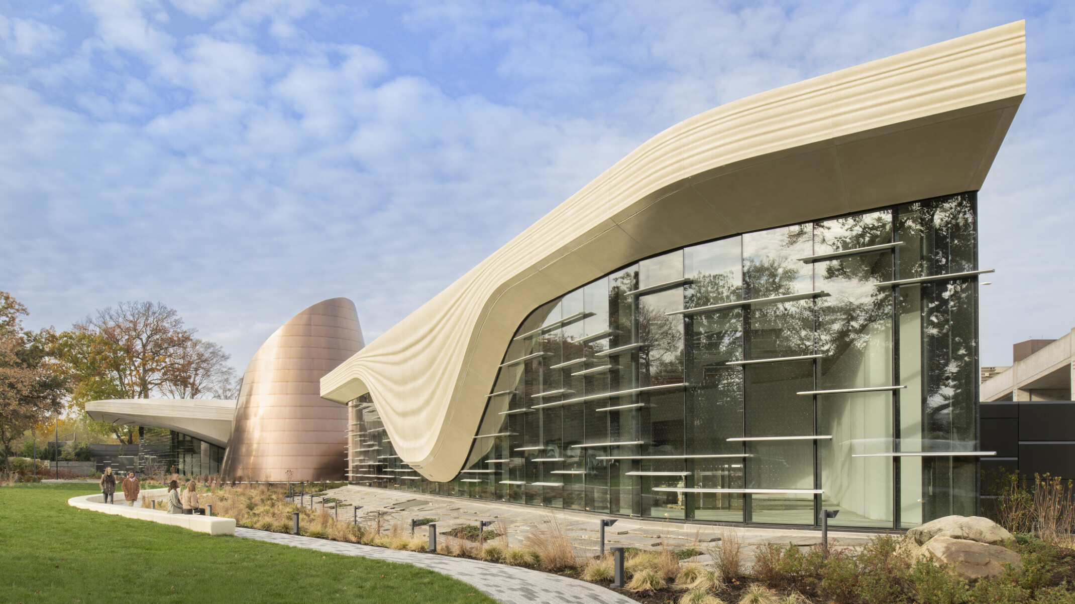 Front facade of the Cleveland Museum of Natrual History; a geometric cream colored concrete structure outlines the large windows of the building to look like a glacier; backdropped by clear blue skies