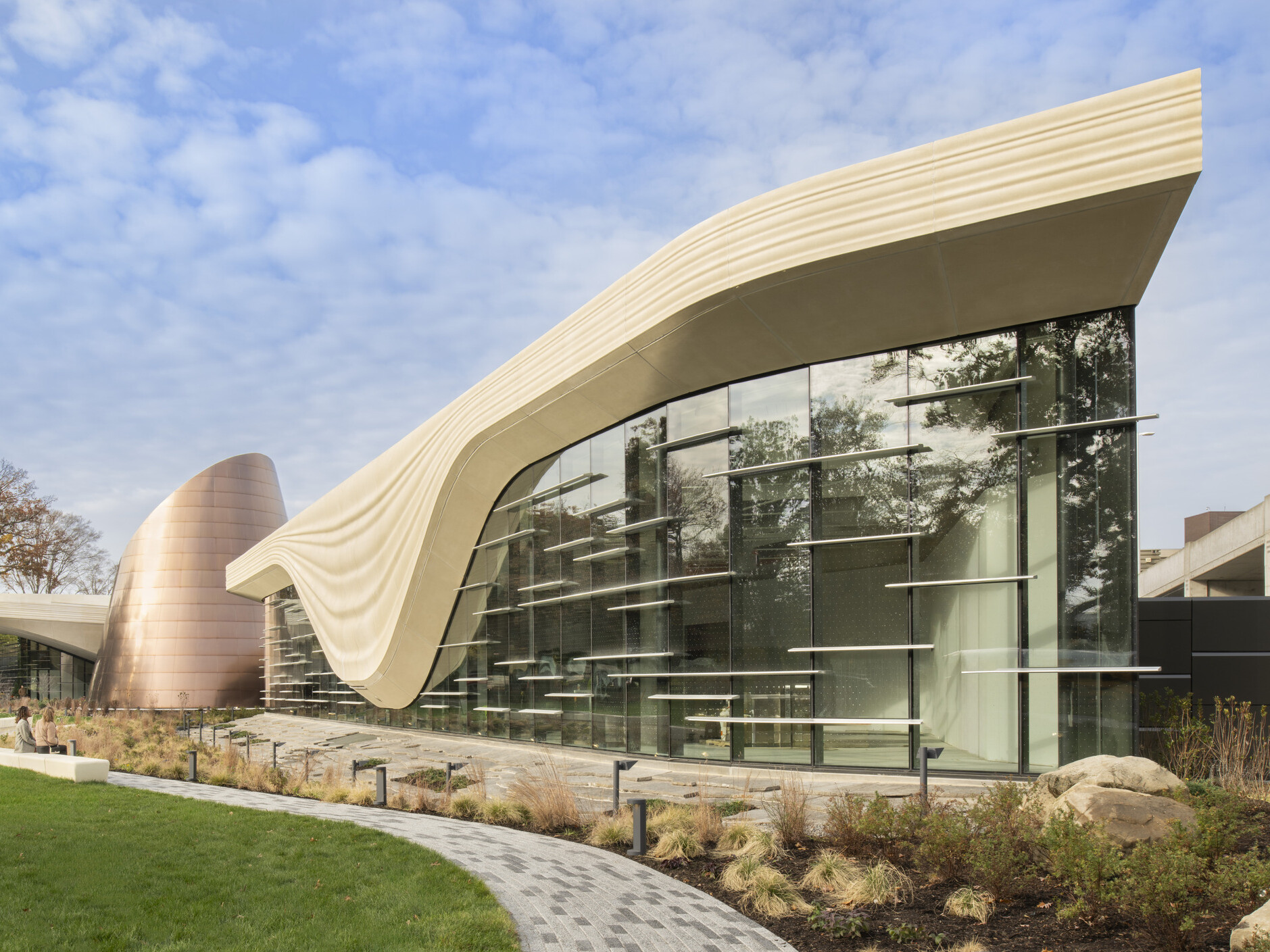 Front facade of the Cleveland Museum of Natrual History; a geometric cream colored concrete structure outlines the large windows of the building to look like a glacier; backdropped by clear blue skies