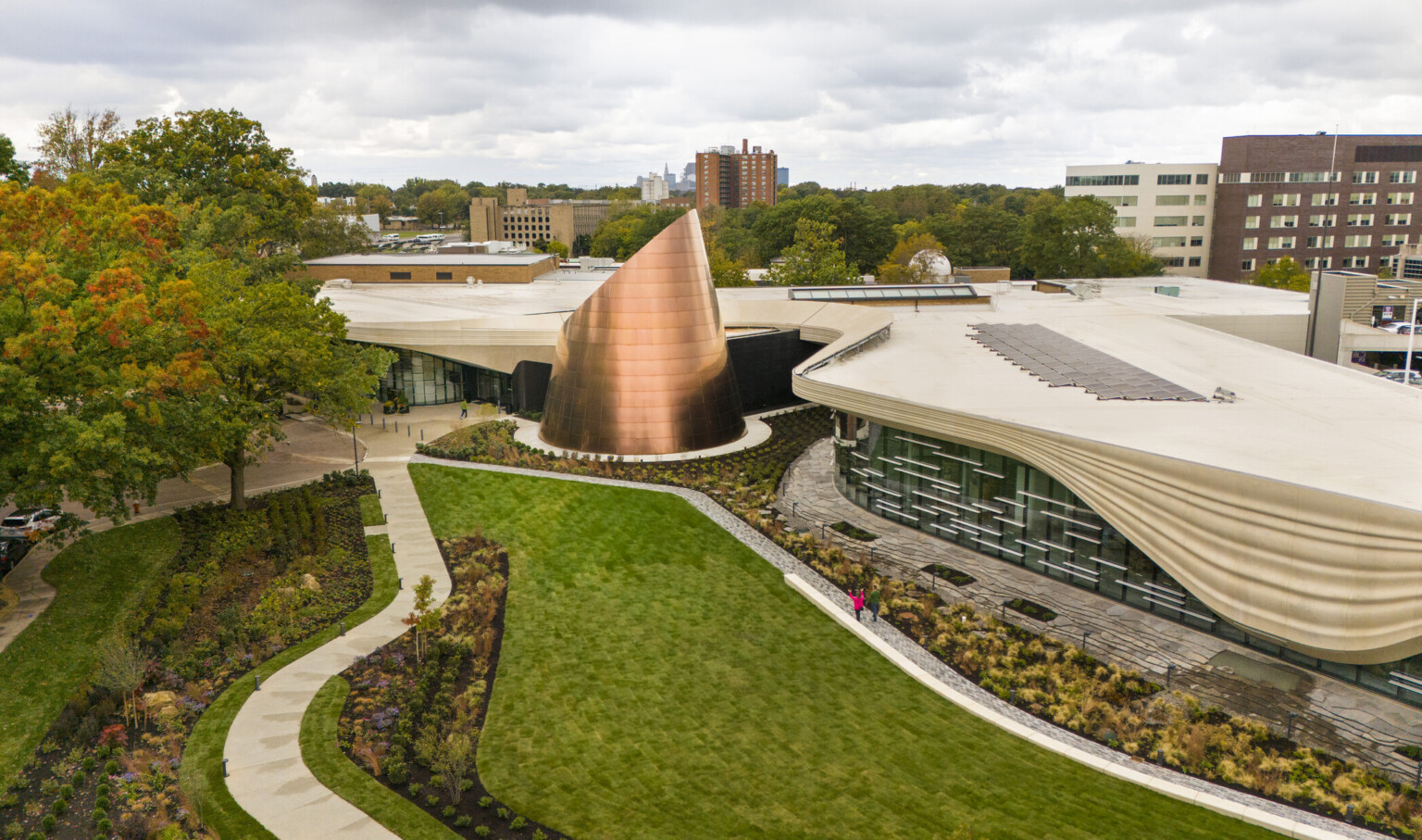 areal view of the Cleveland Museum of Natural History; showcasing the center copper element of the building which is shaped like a glacier; greenery and blue skies surround the building